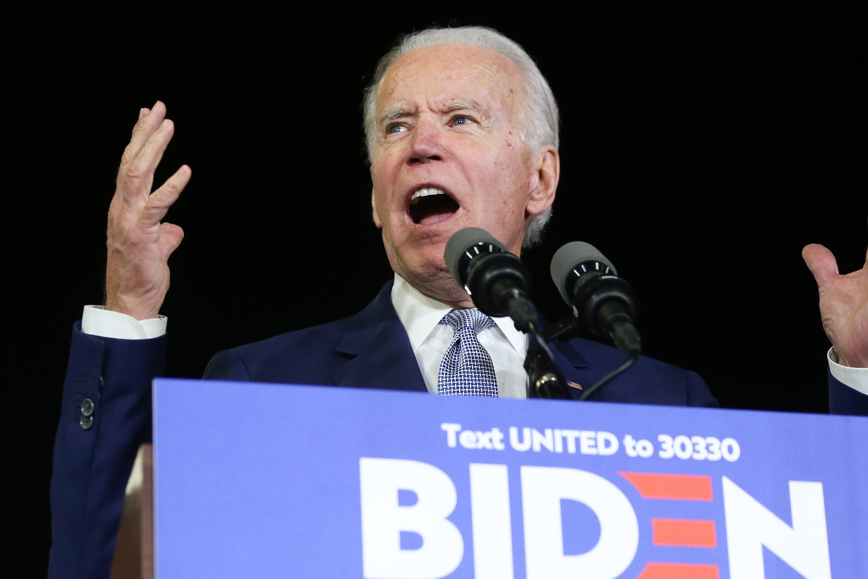 Joe Biden raises his hands while speaking at a podium.