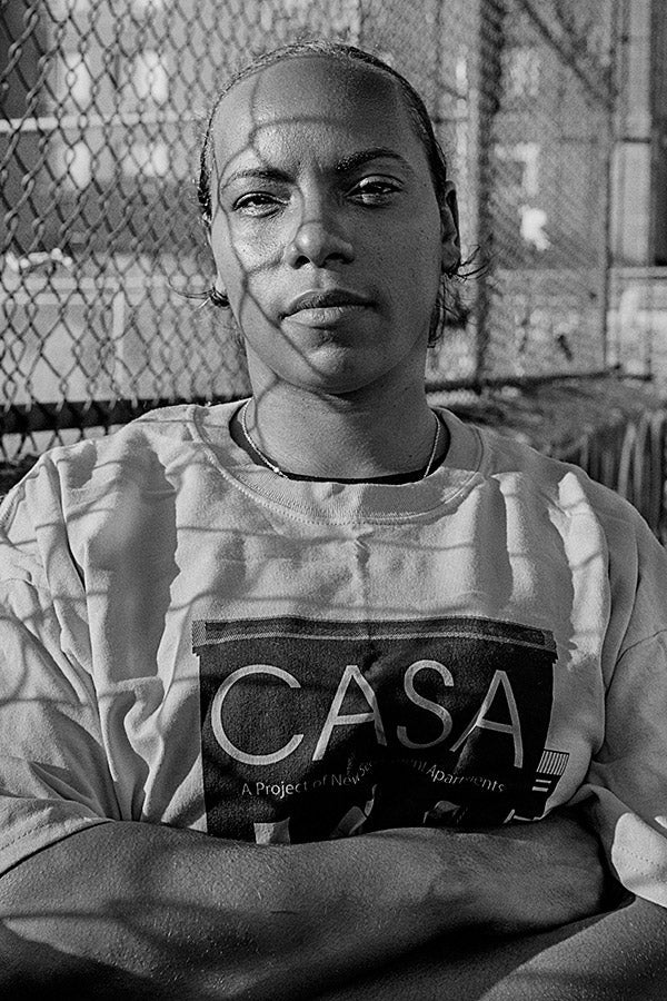 Dulce Infante stands in front of a fence with her arms crossed. Her shirt reads CASA.