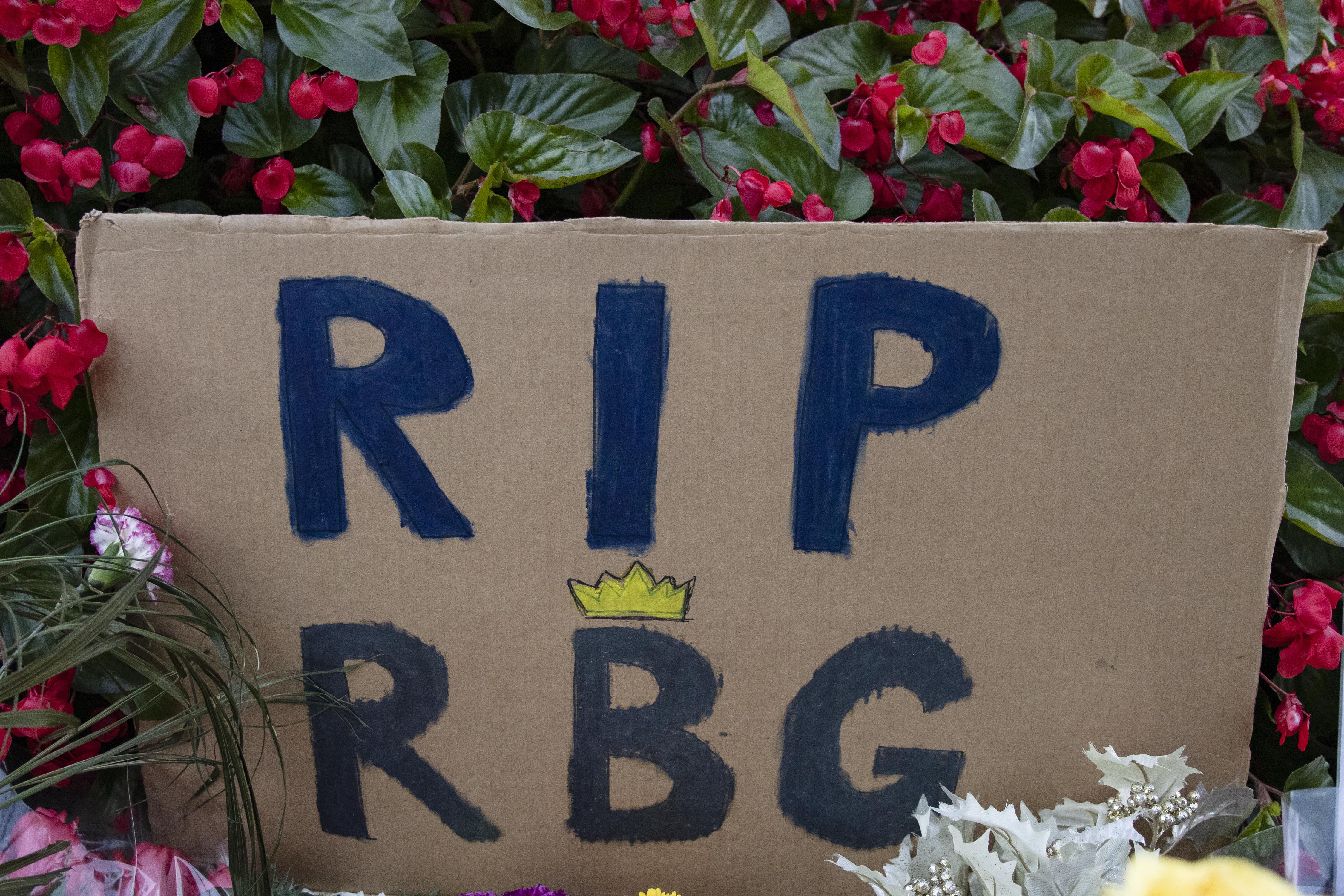 A cardboard sign that reads "RIP RBG," amid flowers