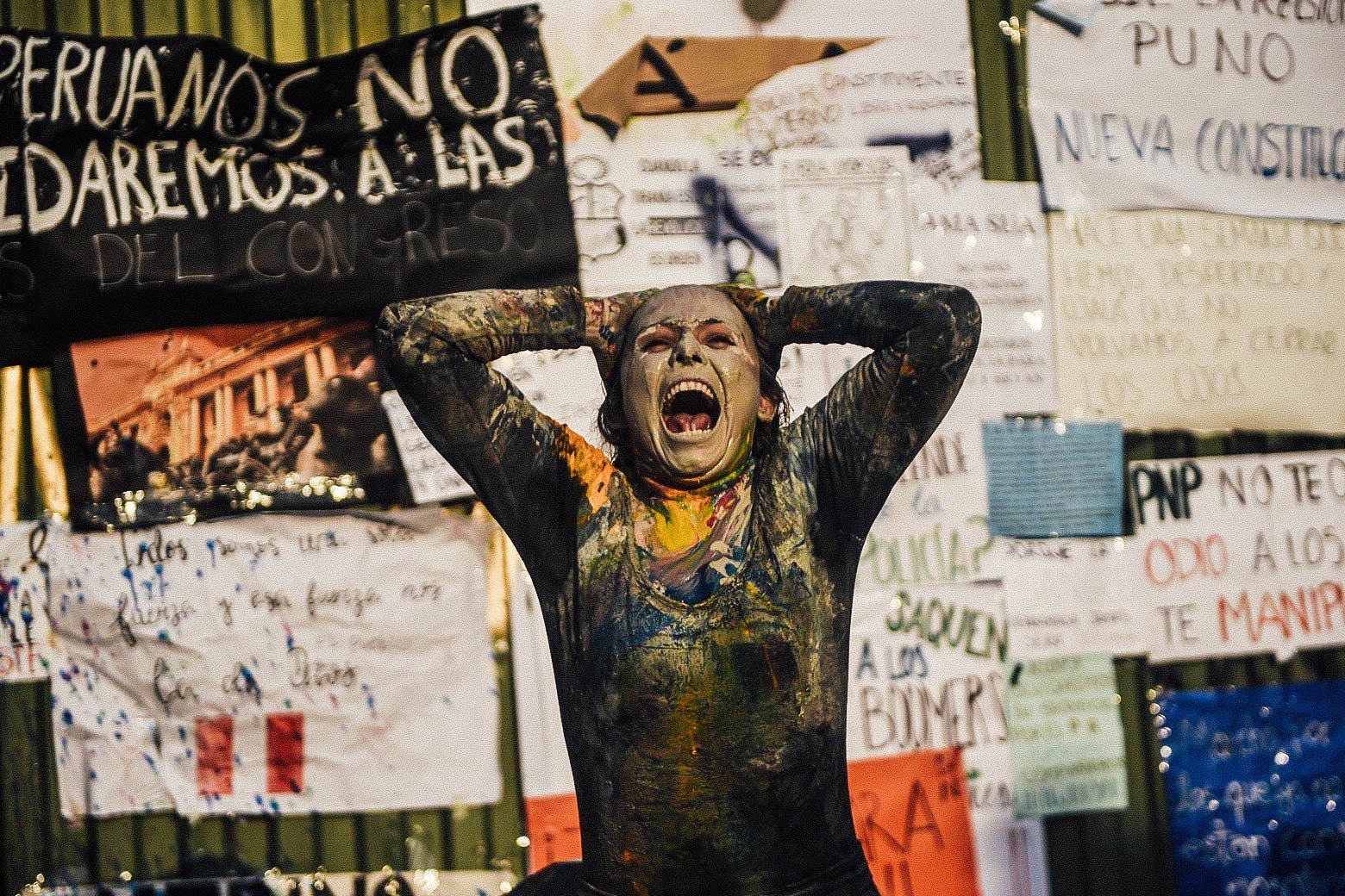 A person covered in paint holds their hands up to their head and tilts back, screaming.
