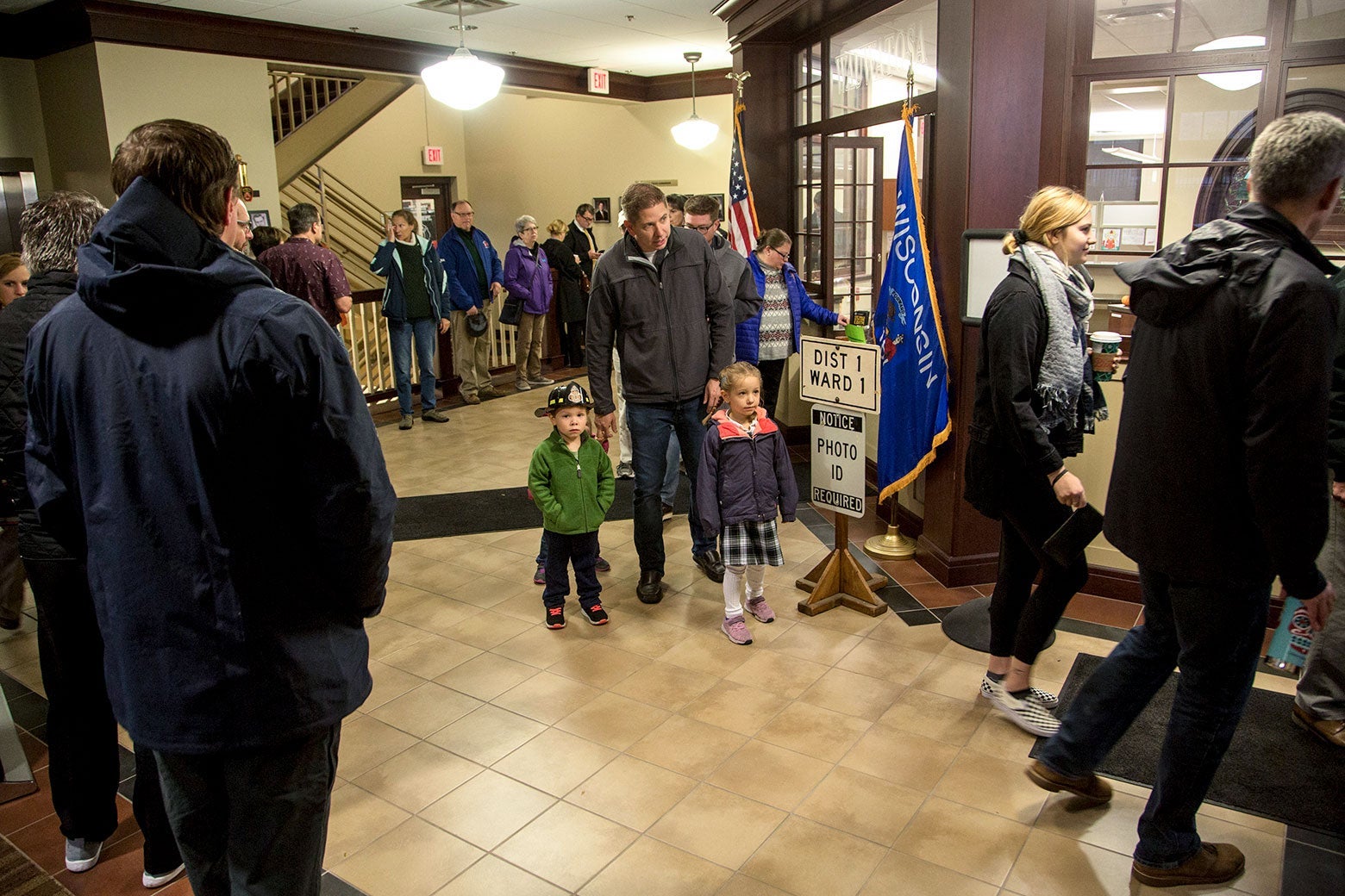 A presumed father stands with two young children while he waits in line to vote.