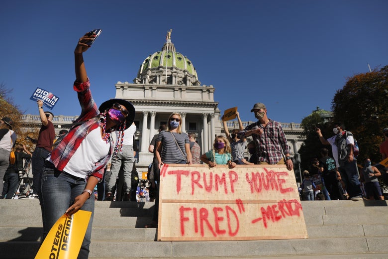 People on the steps of the Capitol take selfies and hold up signs that say "Biden Harris" and "Trump You're Fired"