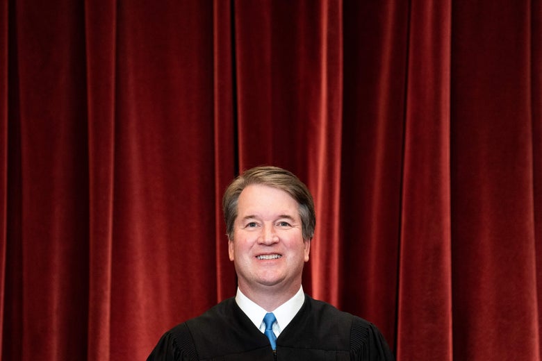 Kavanaugh in his robe smiling with teeth in front of a red velvet curtain