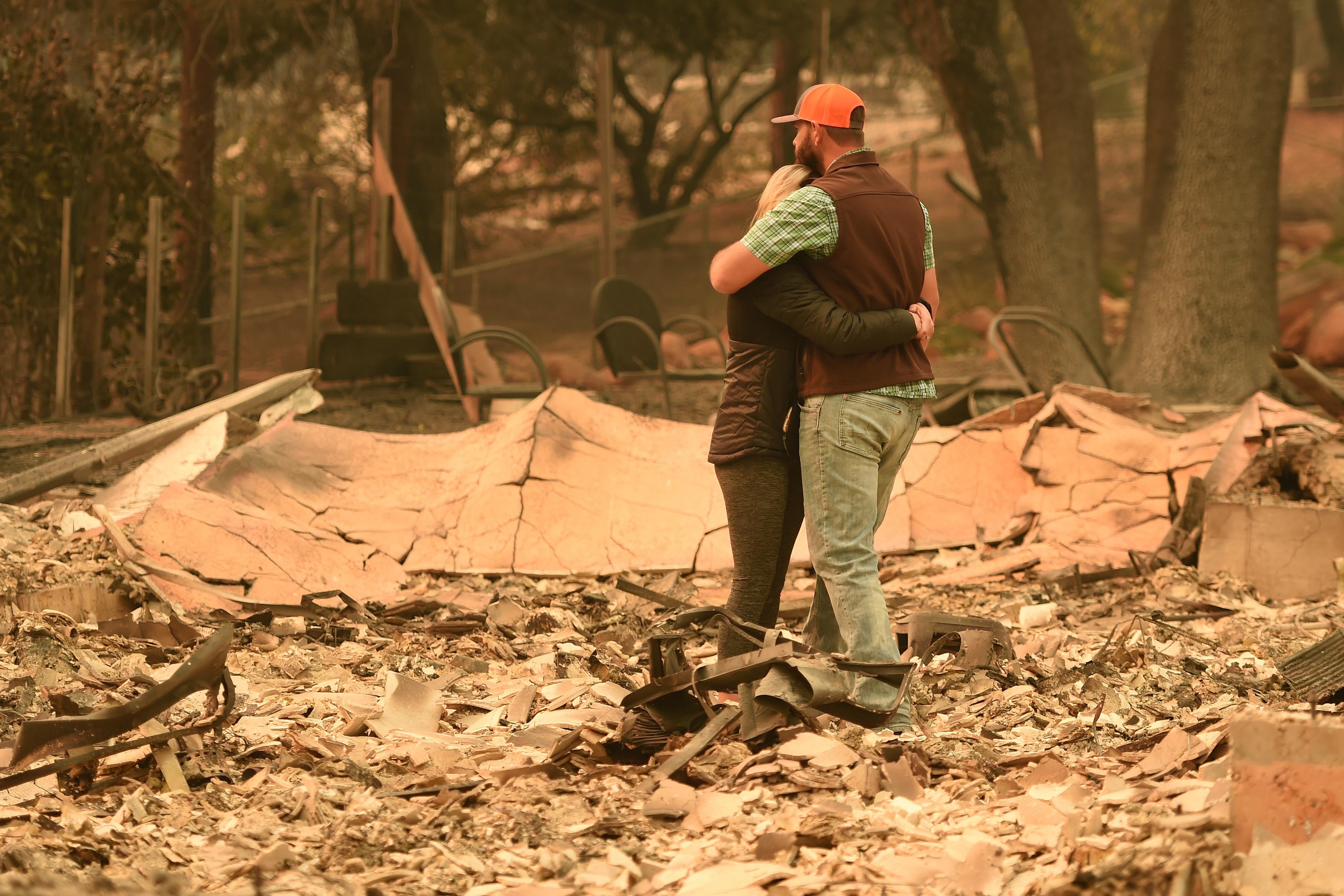 A couple embrace in the middle of the rubble of their home.