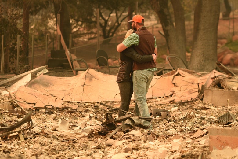 A couple embrace in the middle of the rubble of their home.