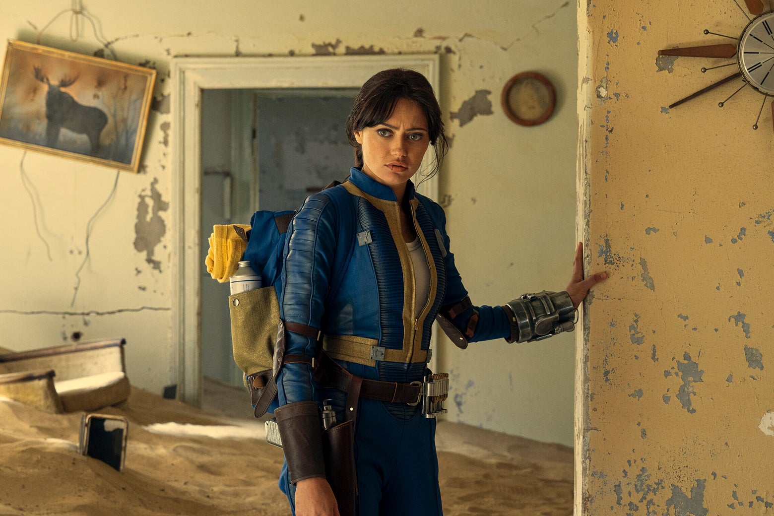 Ella Purnell as Lucy, standing in an abandoned house overtaken by desert.
