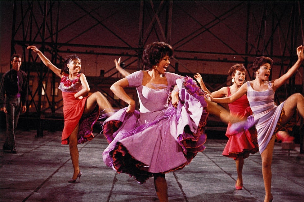 Rita Moreno leads a group of high-kicking women in brightly colored dresses.
