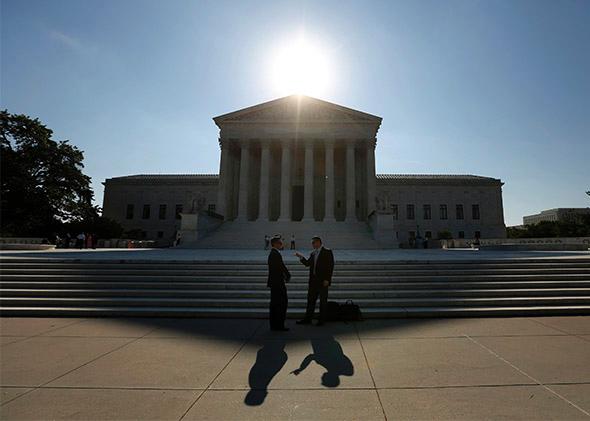 Two men talk as the sun rises over the Supreme Court.