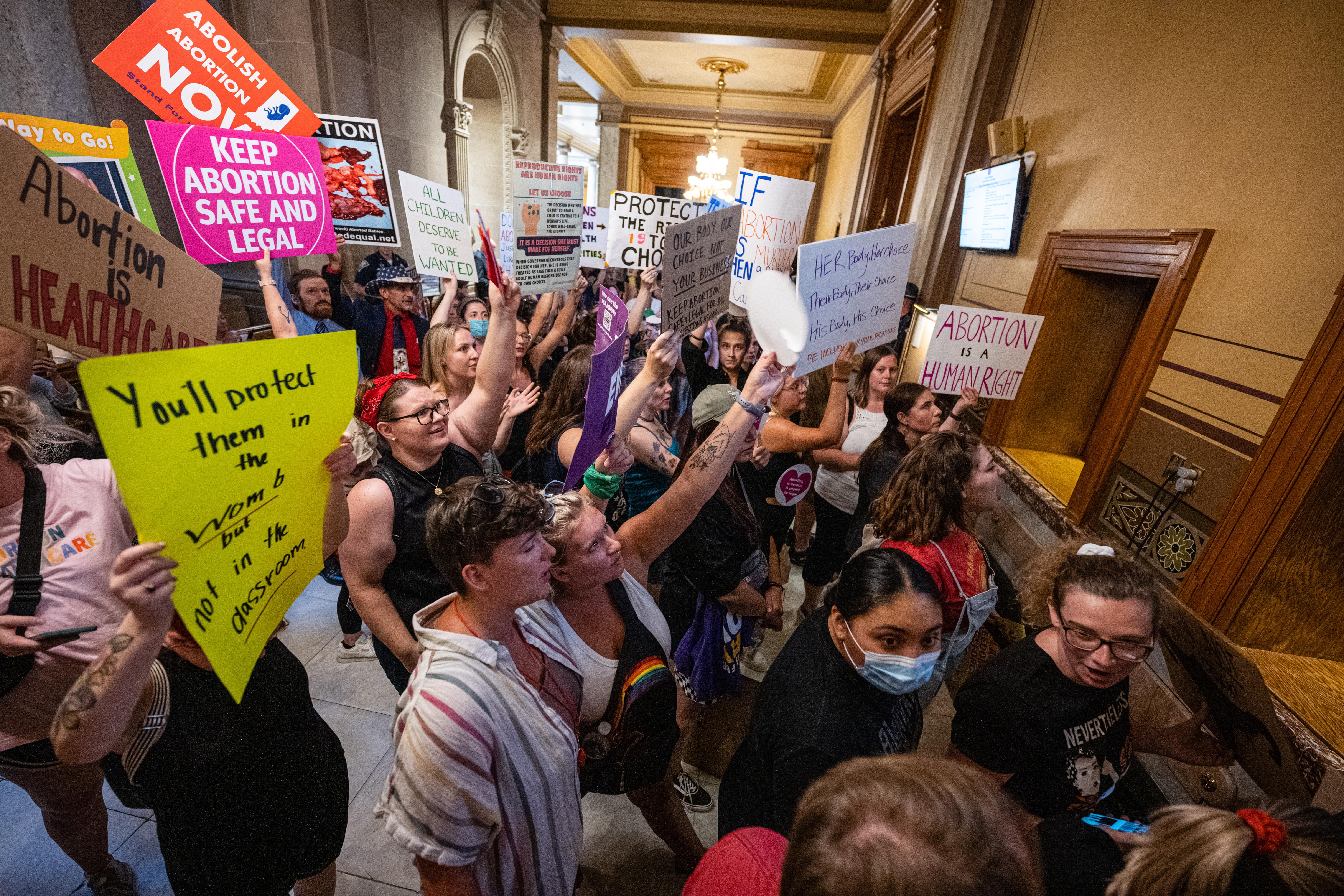 Dozens of abortion protesters carry signs in a hallway of a state legislature. 