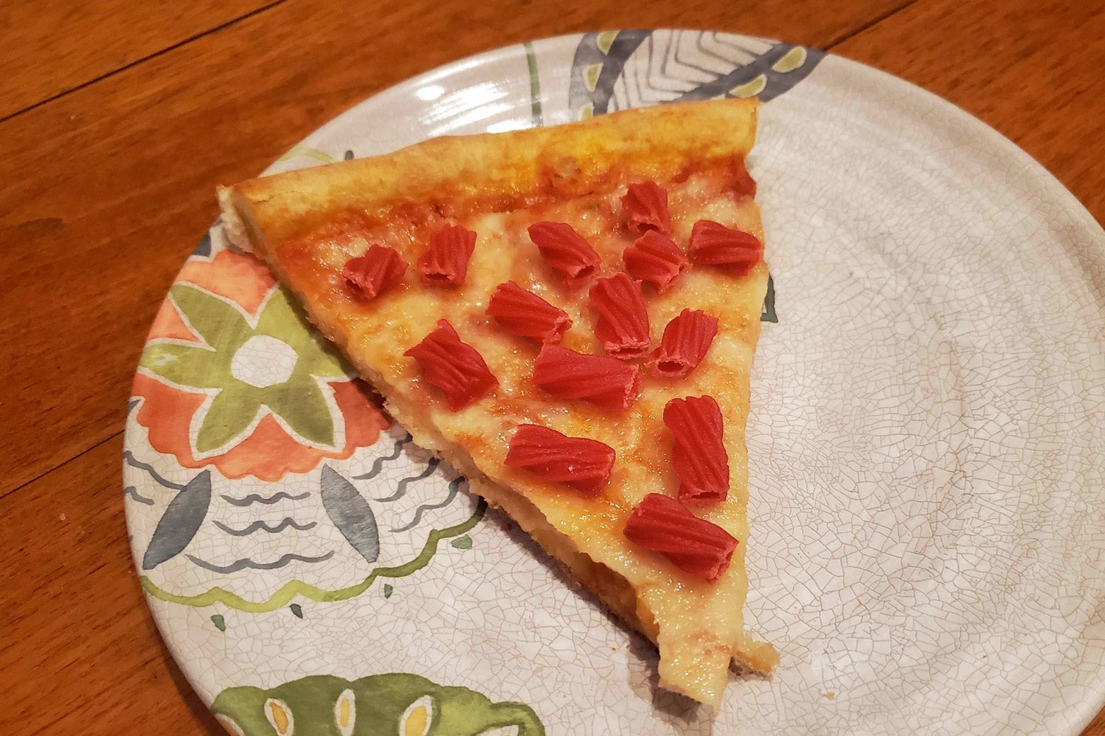 A slice of cheese pizza with longer slices of red licorice on it.