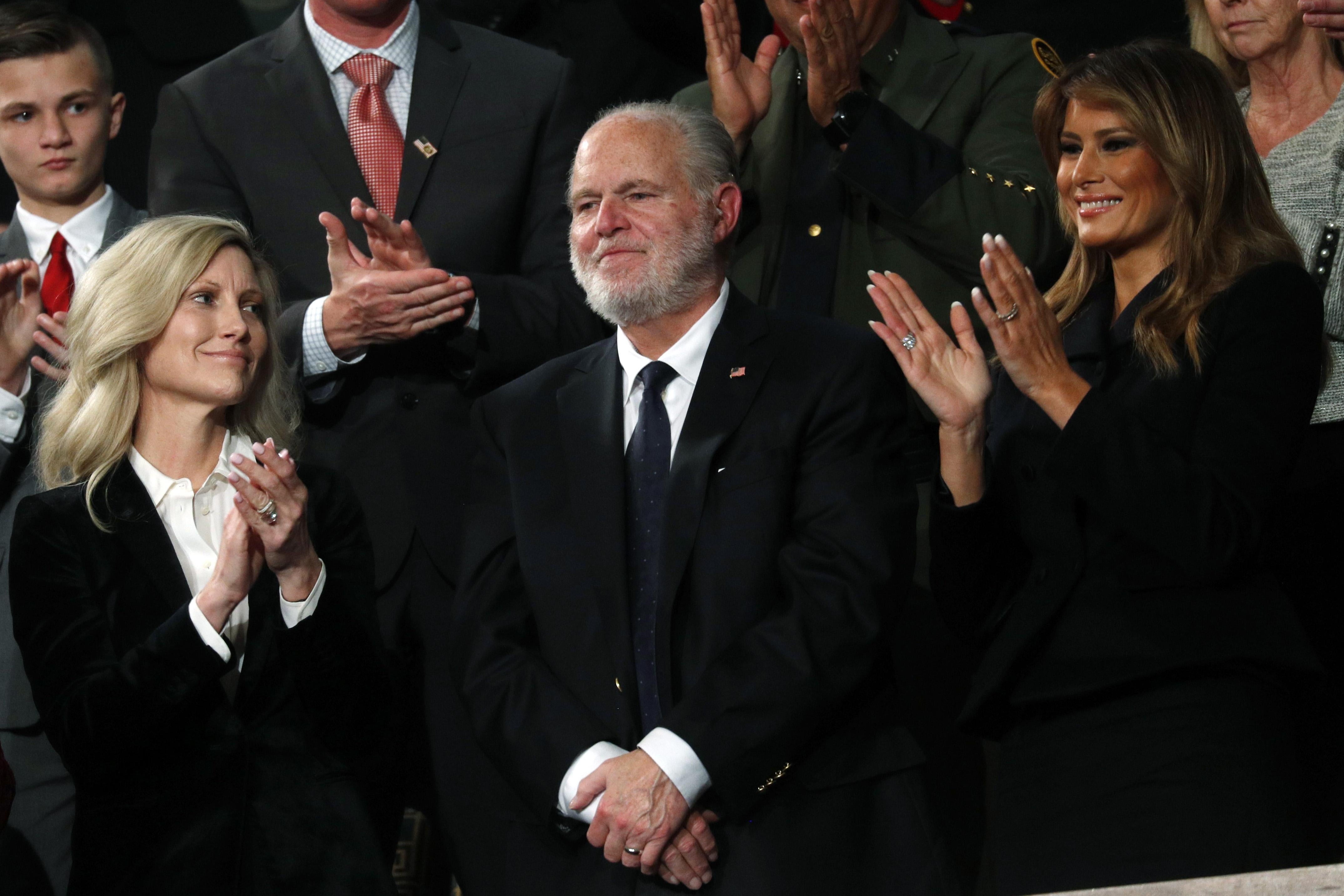 Limbaugh smiles as his wife, Kathryn, and Melania Trump clap beside him.