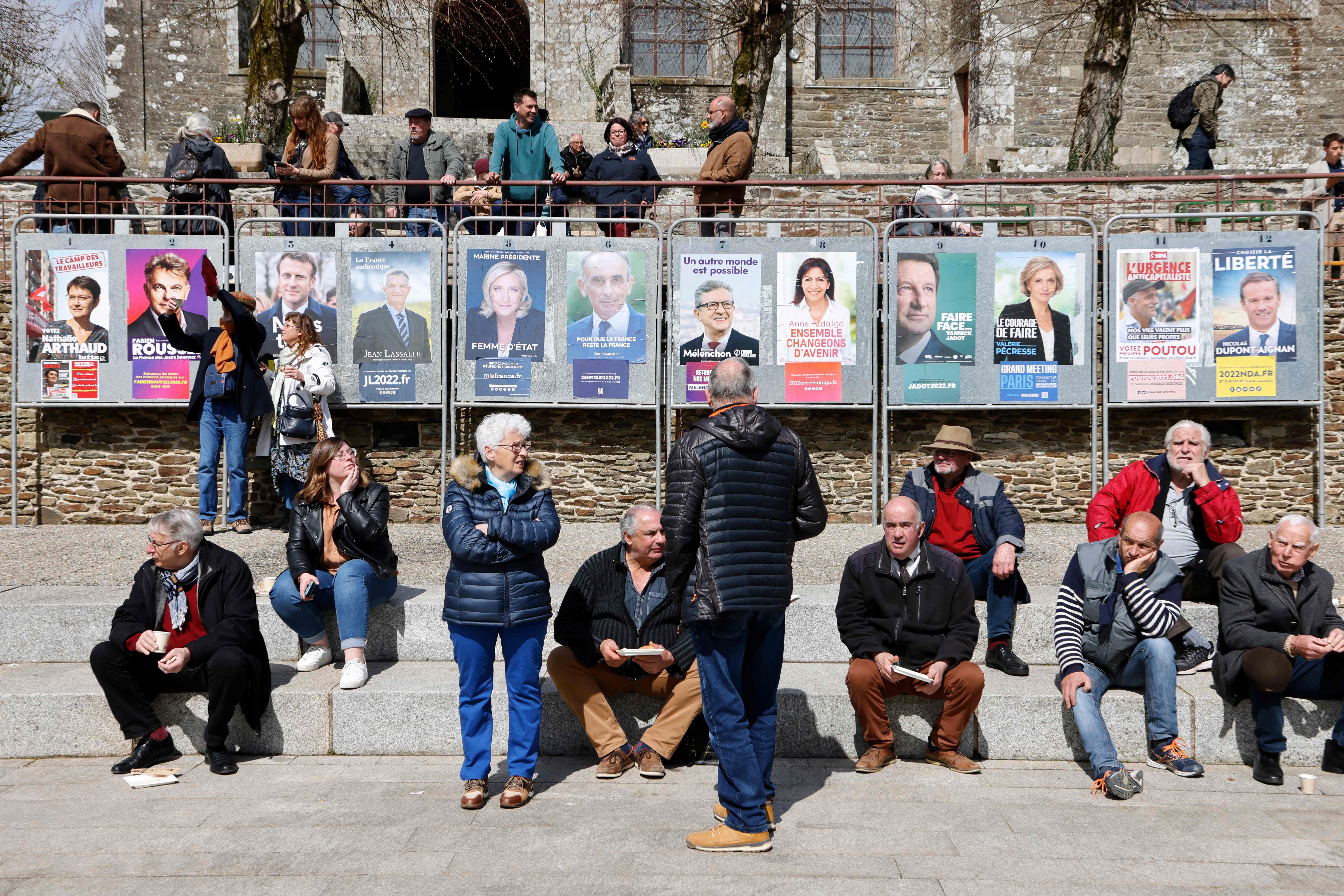 Local residents stand on the main square, next to the 12 official posters of presidential candidates, during the visit of French President and liberal party La Republique en Marche (LREM) candidate for re-election Emmanuel Macron in Spezet, western France, on Tuesday. 