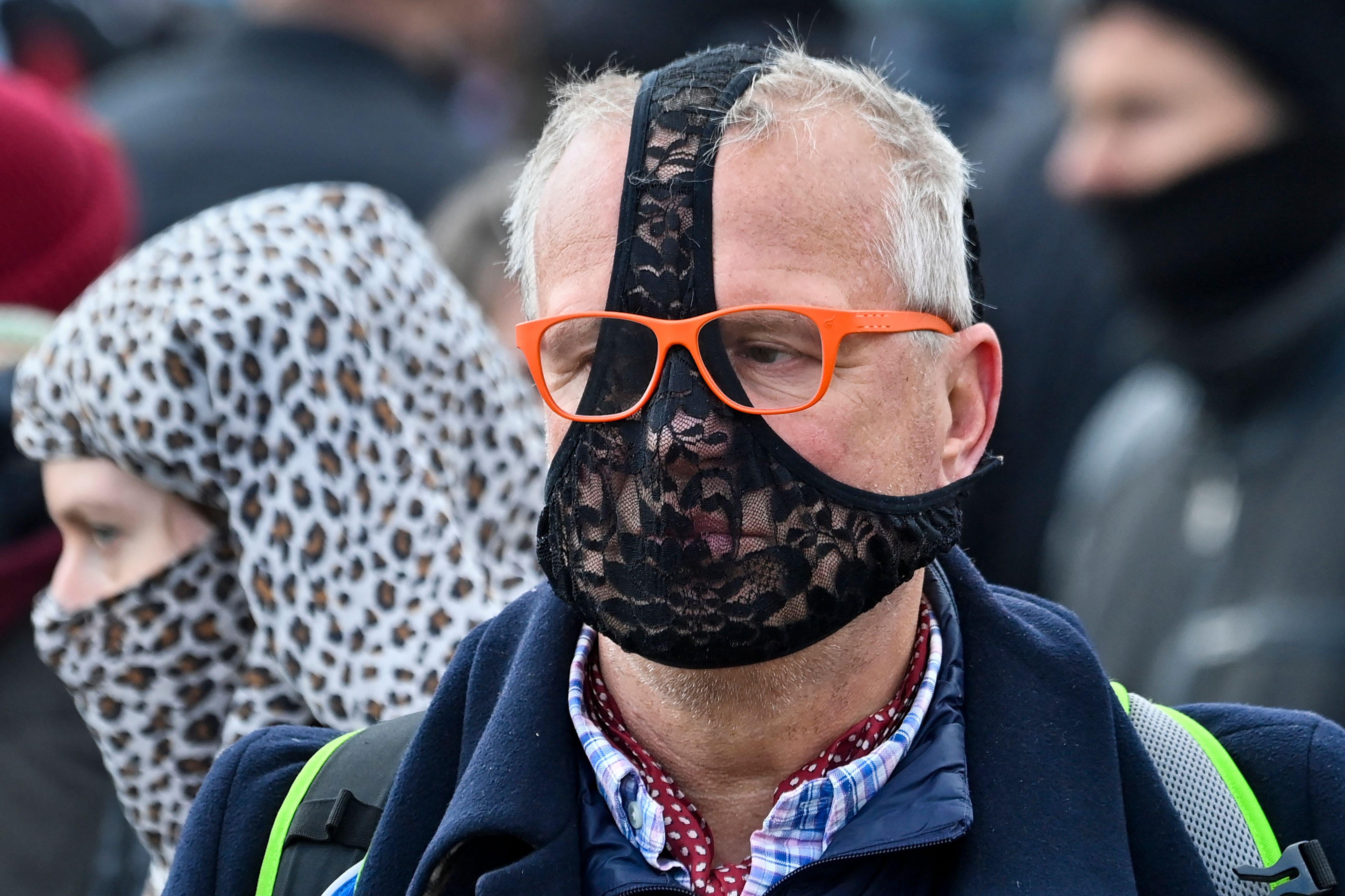 An older man wears black lacy underwear over his face.