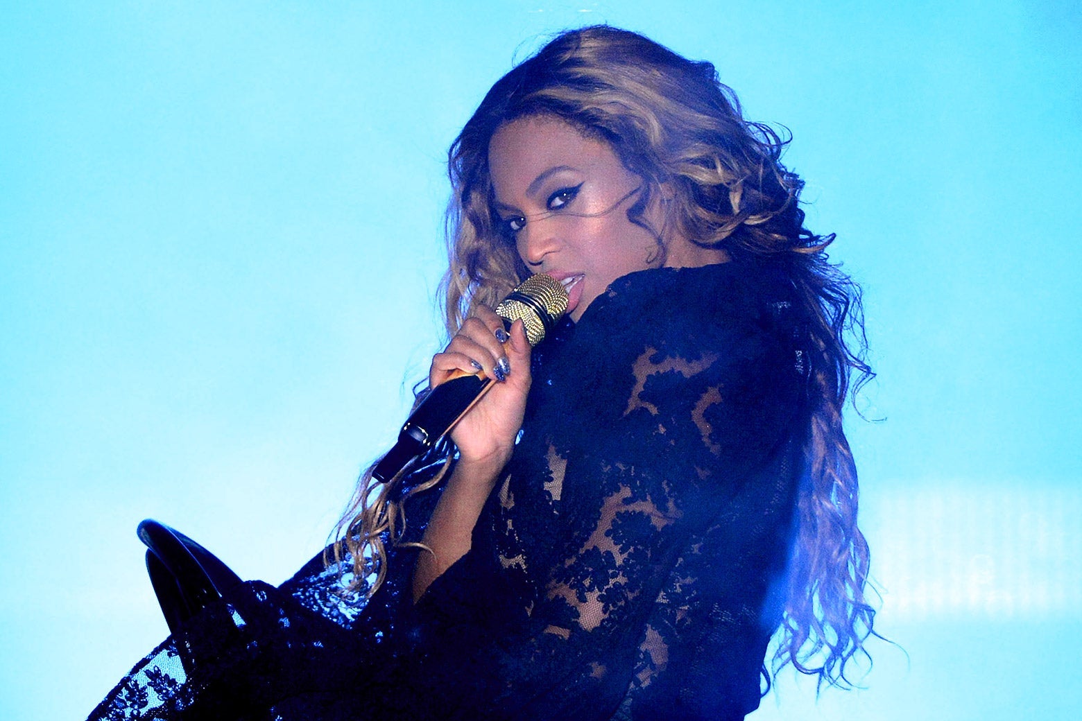 Beyoncé looks over her shoulder, singing into a gold microphone.