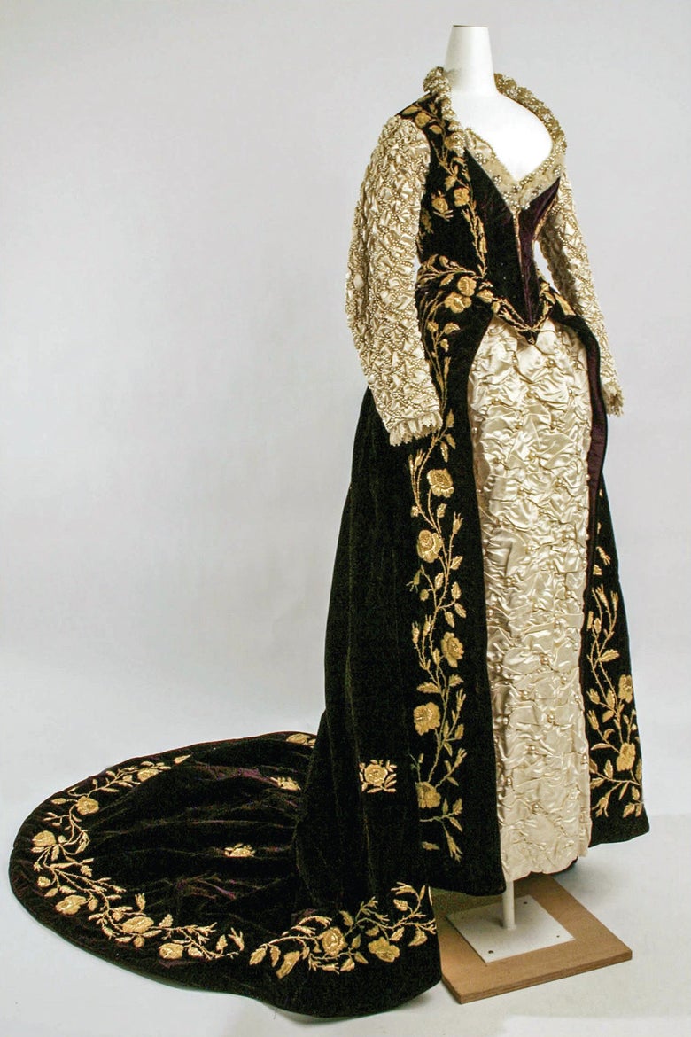 An elaborate gown featuring gold embroidery, with an open front and a train. 