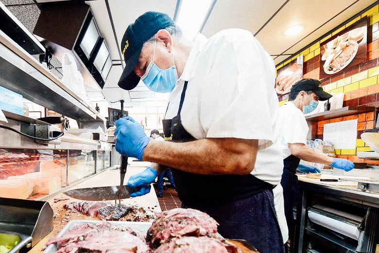 Men wear facemasks as they slice meat and perform other tasks.