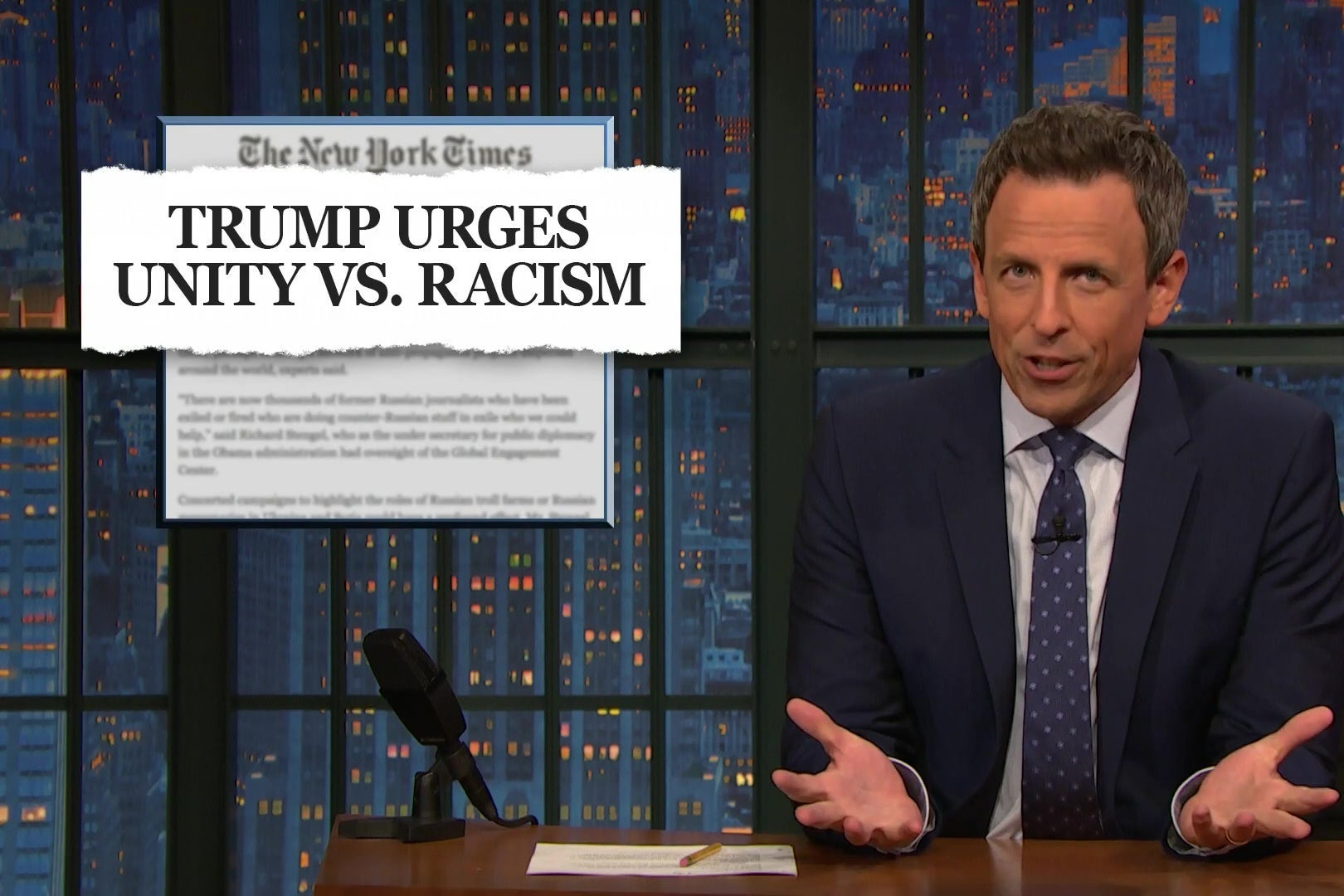 Seth Meyers gestures in disbelief in front of a New York Times headline reading "TRUMP URGES UNITY VS. RACISM."