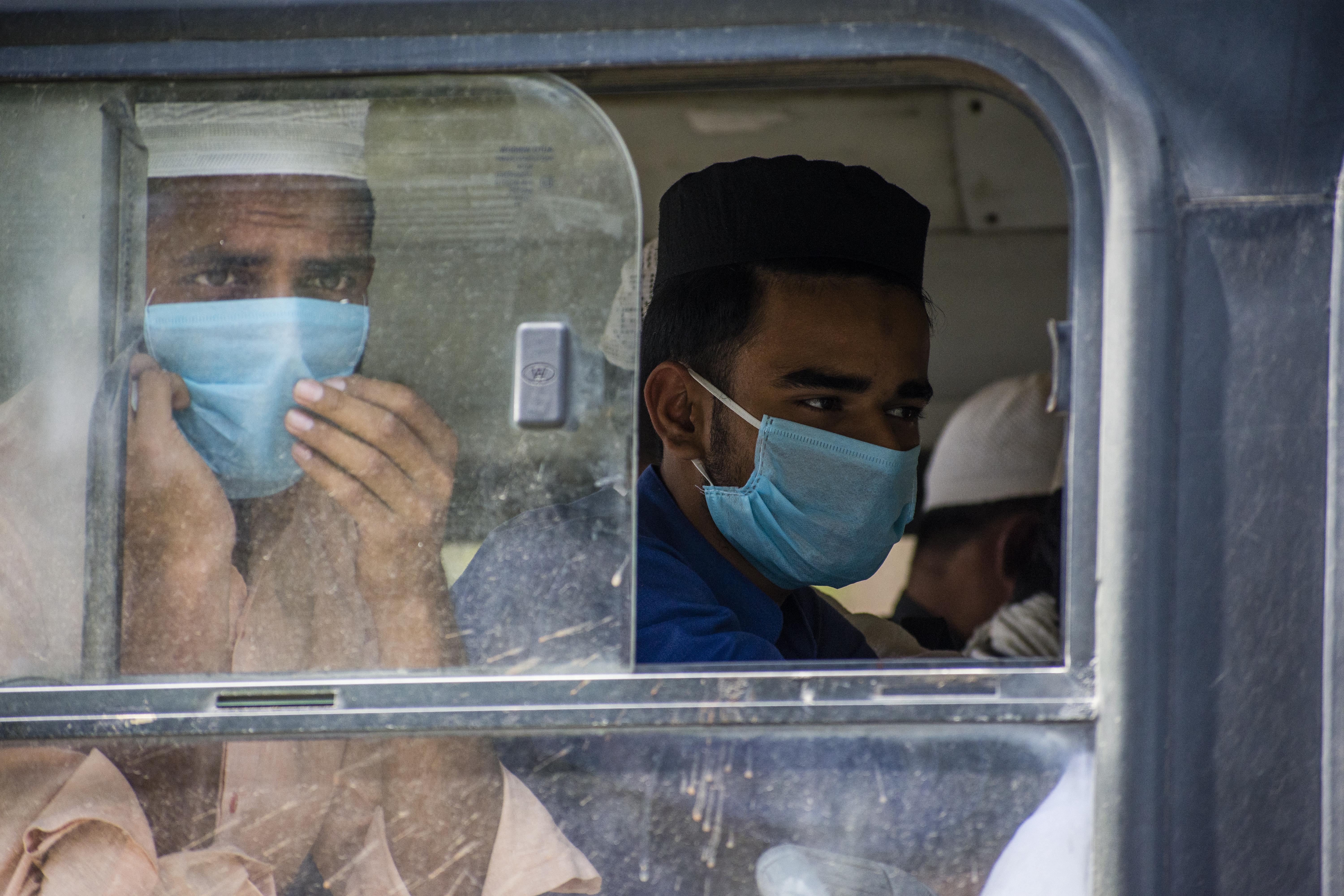 Men wearing surgical masks look out the window of a bus