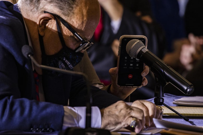 Rudy Giuliani listens as Jenna Ellis, both members of President Donald Trump's legal team, holds up a cellphone to the microphone so President Trump can speak during a hearing.