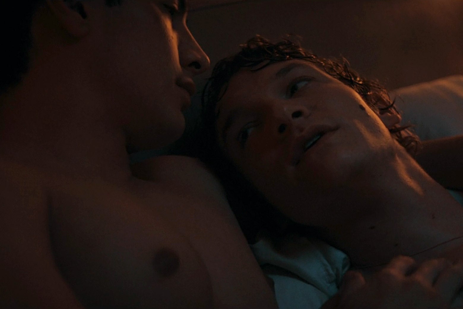 Two men share a postcoital embrace in a bed.
