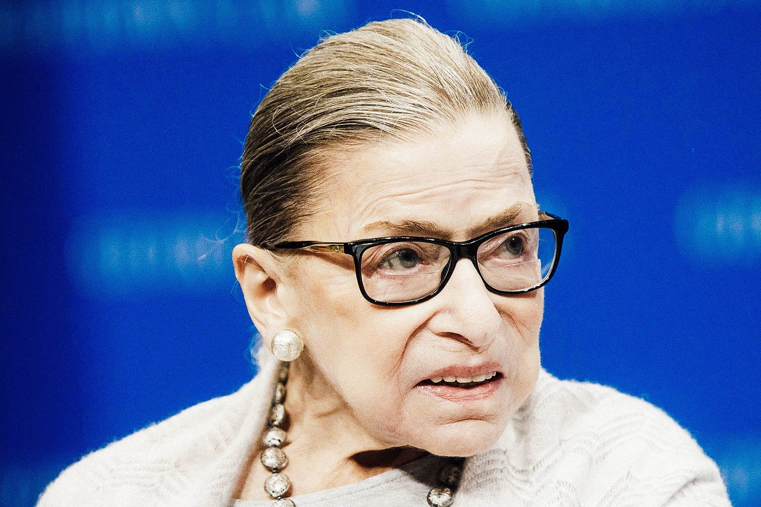 Ruth Bader Ginsburg looks to her side. There is a blue background.