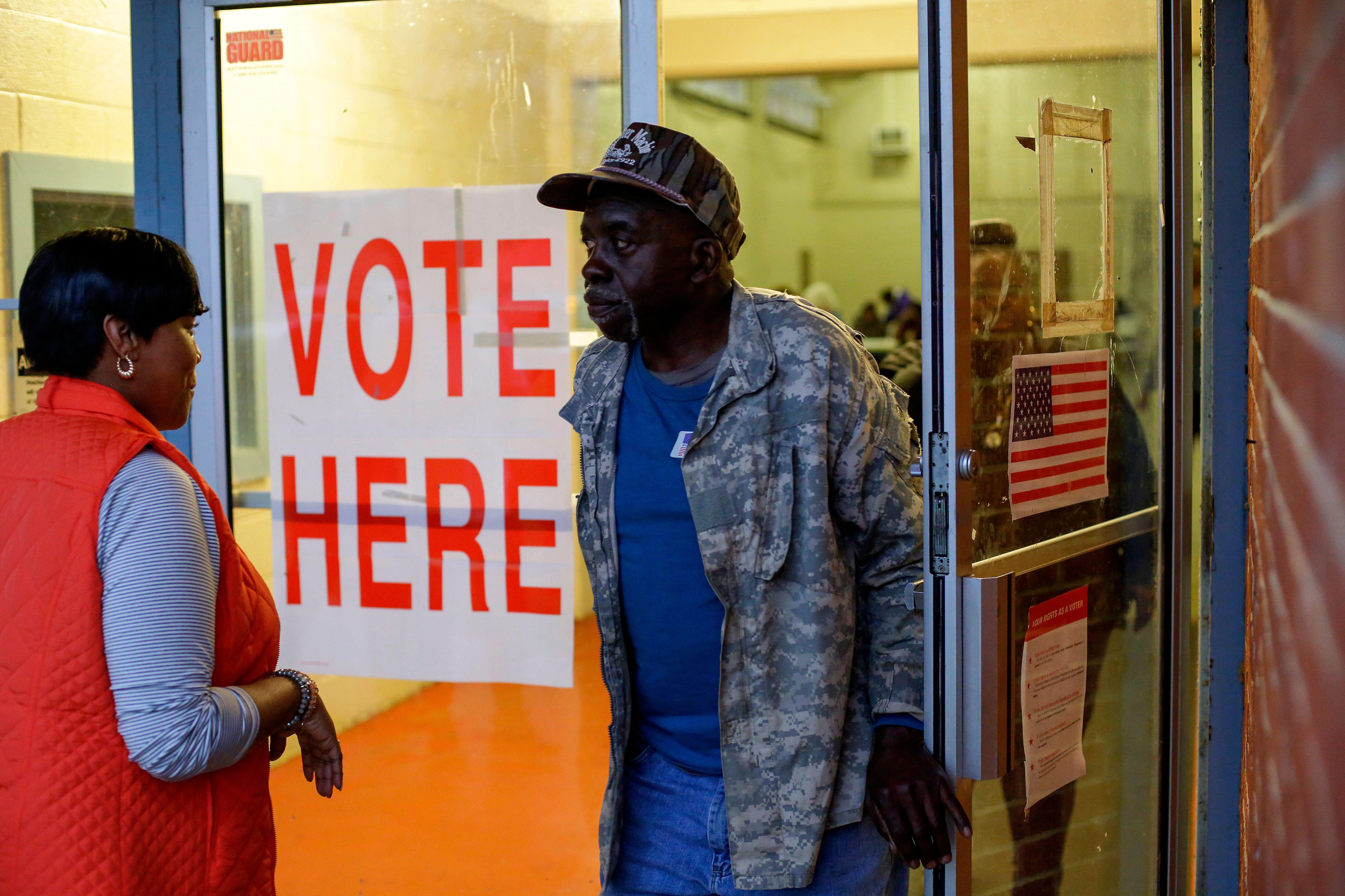 A Black man walks out of a building where it says VOTE HERE on the door.
