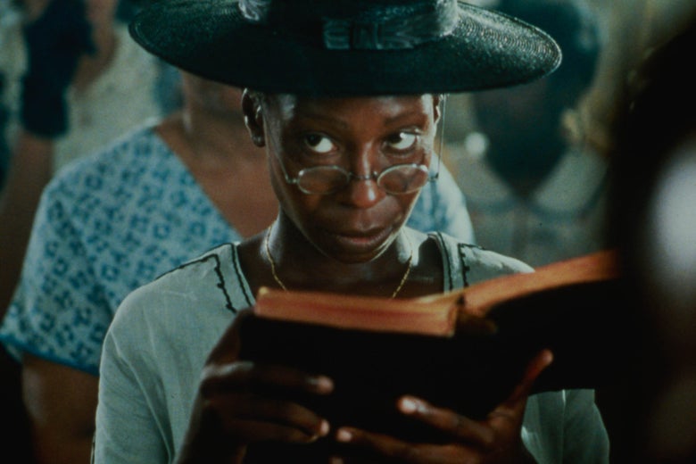A black woman in a large black hat sits in a church pew looking over her glasses at something off-screen while holding a bible in her hands.