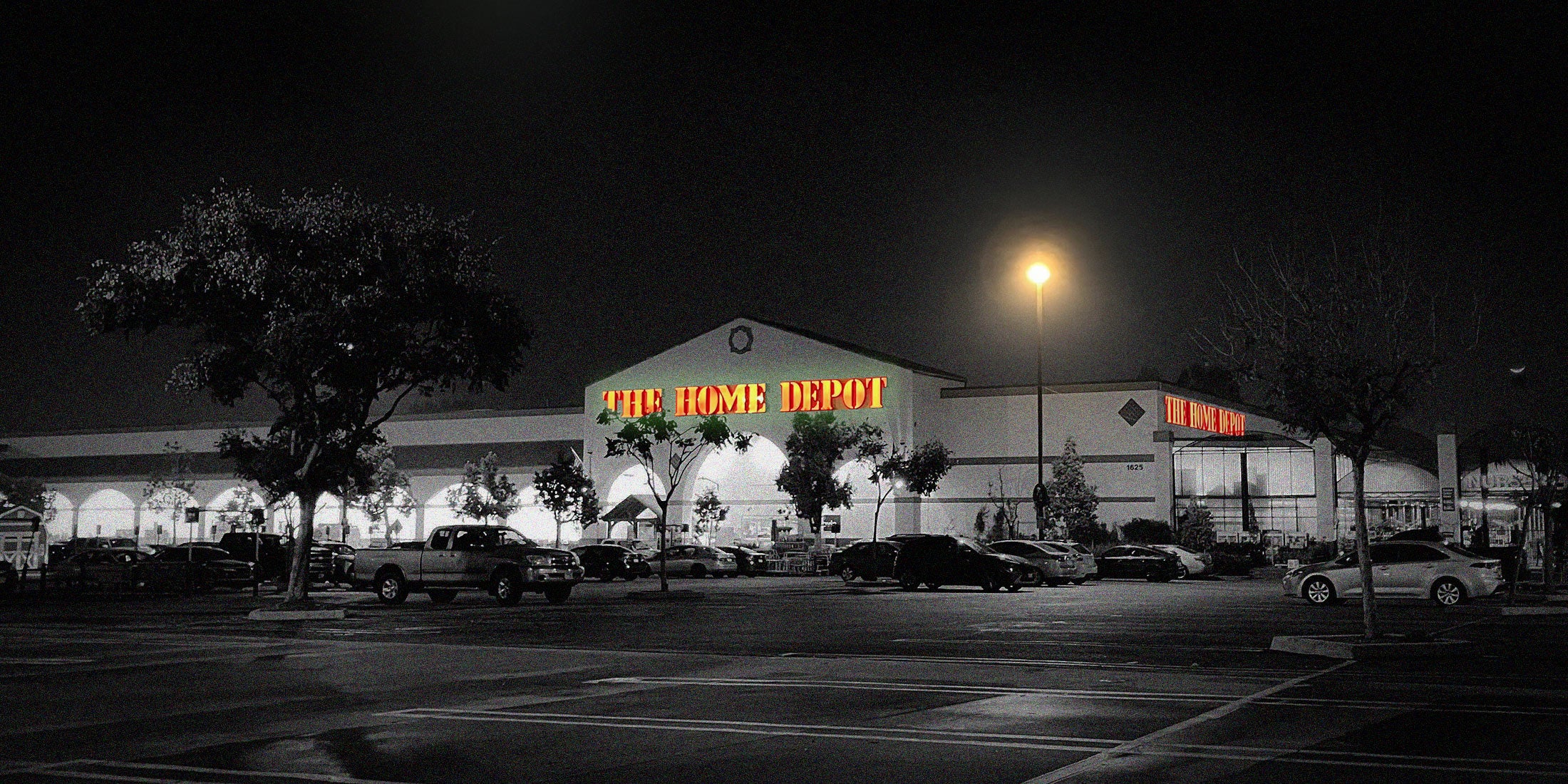 A quiet Home Depot parking lot at night is black and white except for one lamp and the orange sign.