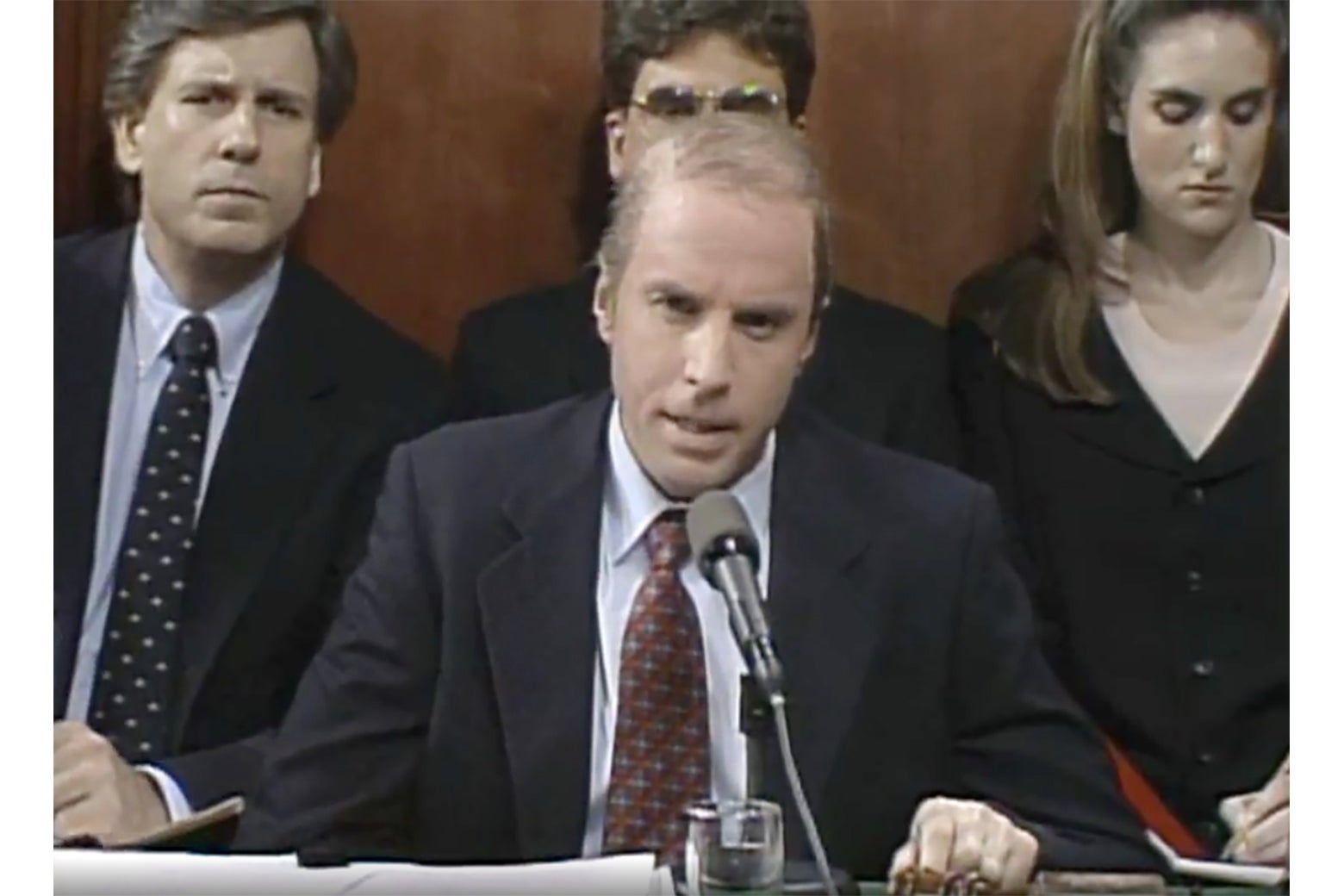 Kevin Nealon as Joe Biden, sitting behind a microphone, on SNL. Three others sit behind him.