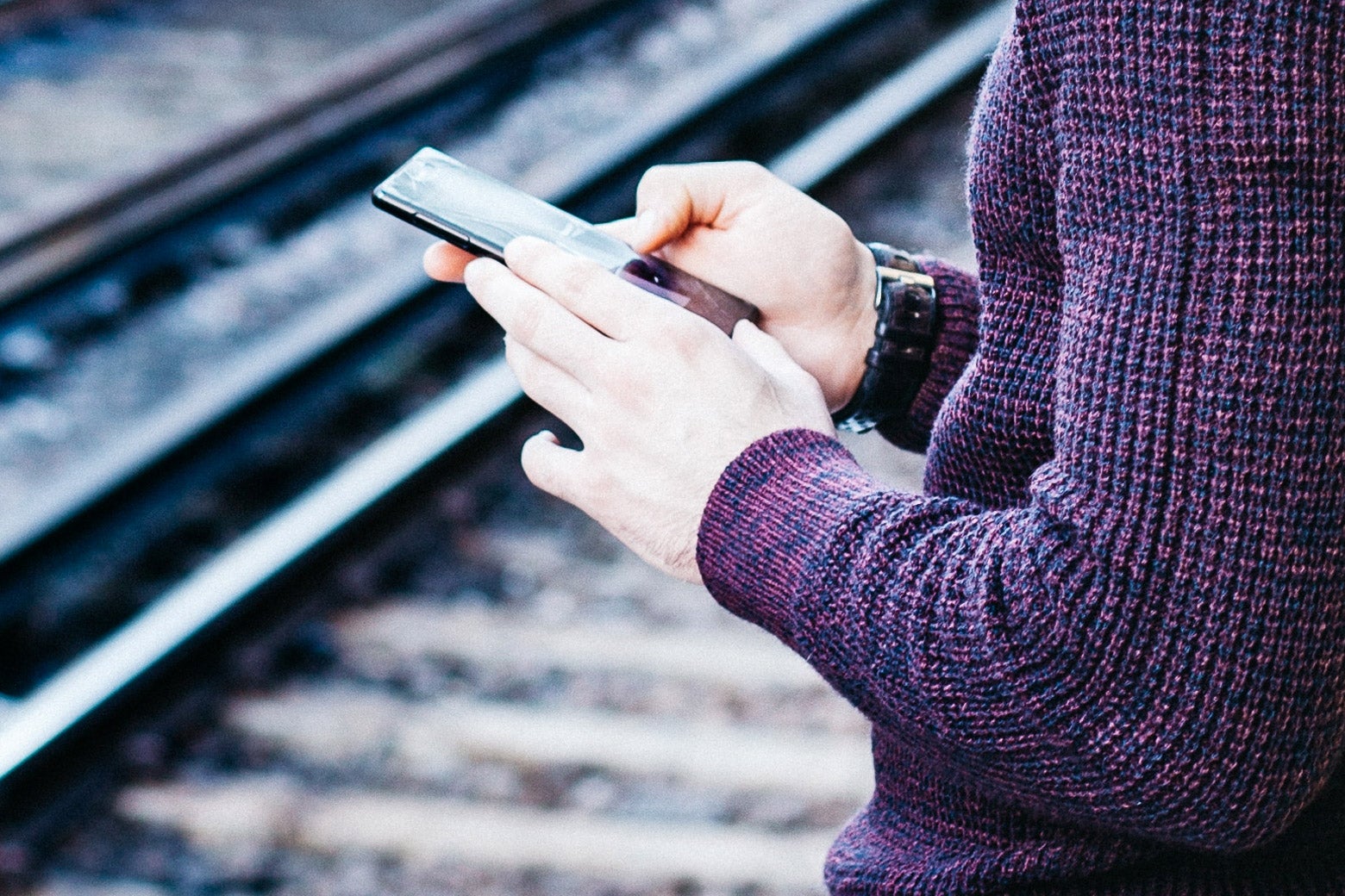 A man types on his phone while waiting for a train.