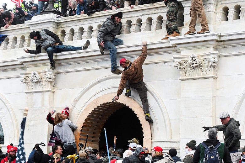 Multiple pro-Trump rioters climb up the walls of the U.S. Capitol while others congregate nearby.