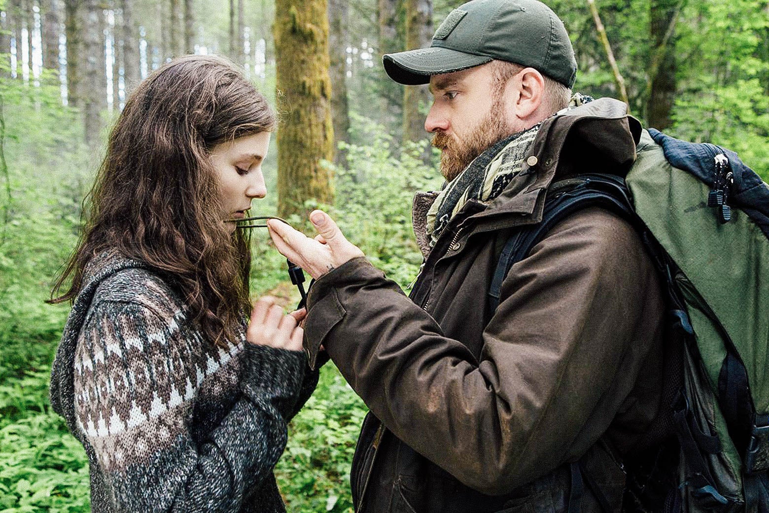 Movie still: Thomasin McKenzie stands while Ben Foster tugs at an object around her neck.
