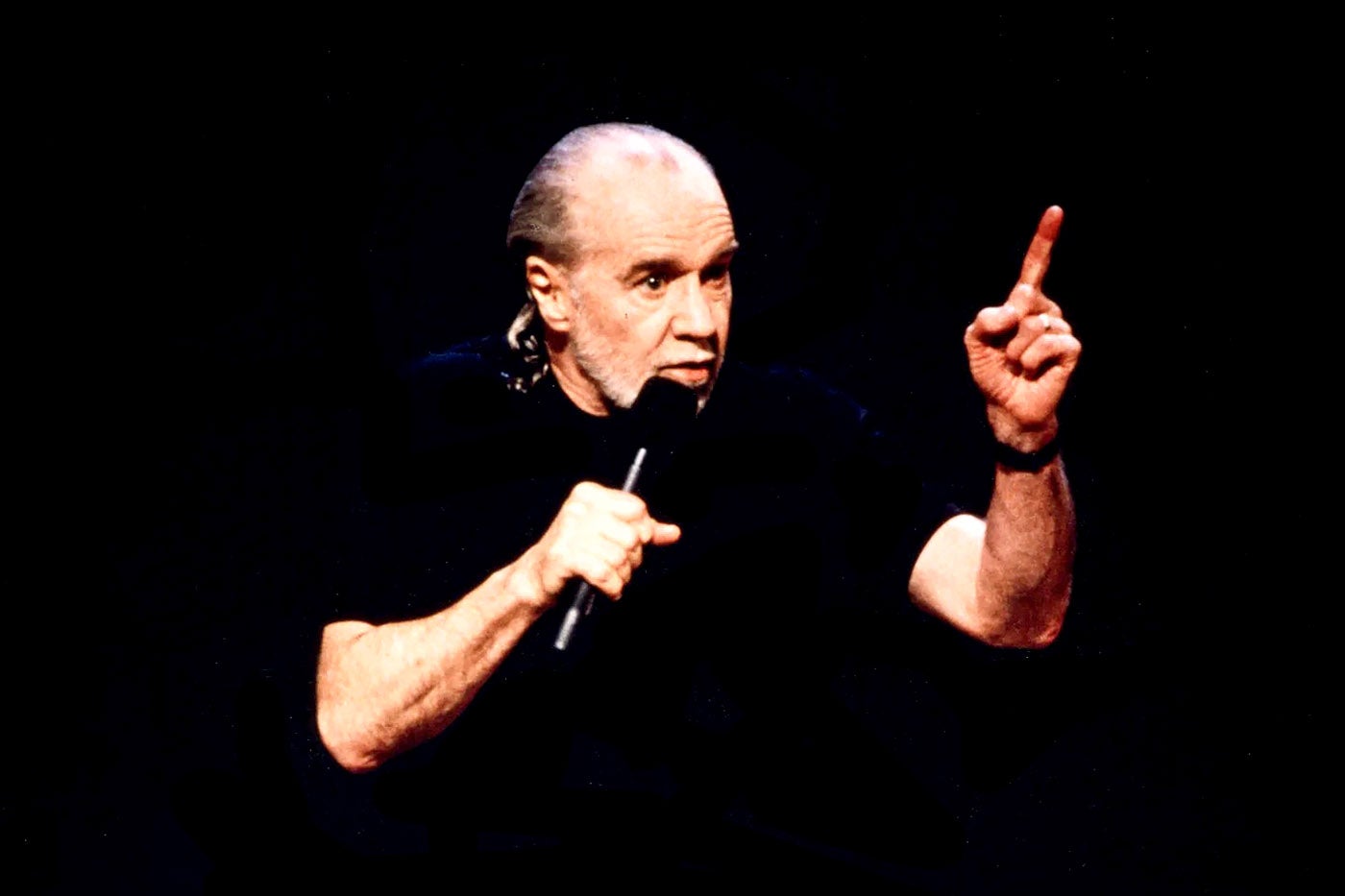 George Carlin on stage in a black t-shirt.