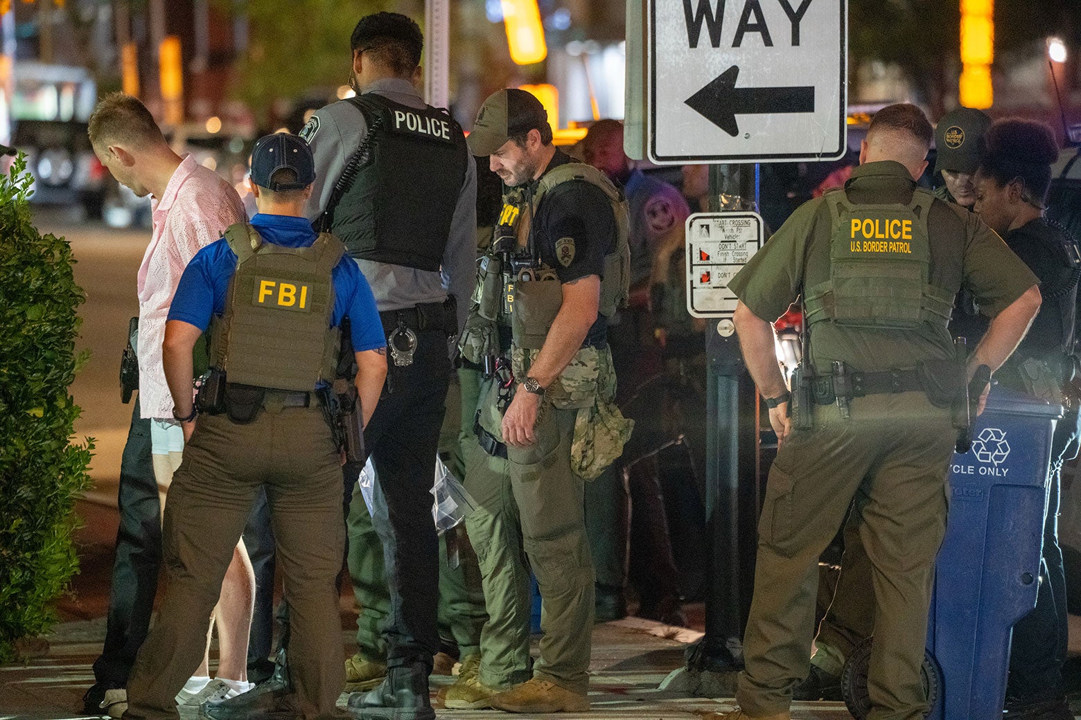 Multiple FBI and Border Patrol officers handcuff and arrest a thirtysomething man in a pink button-down shirt on a city street.