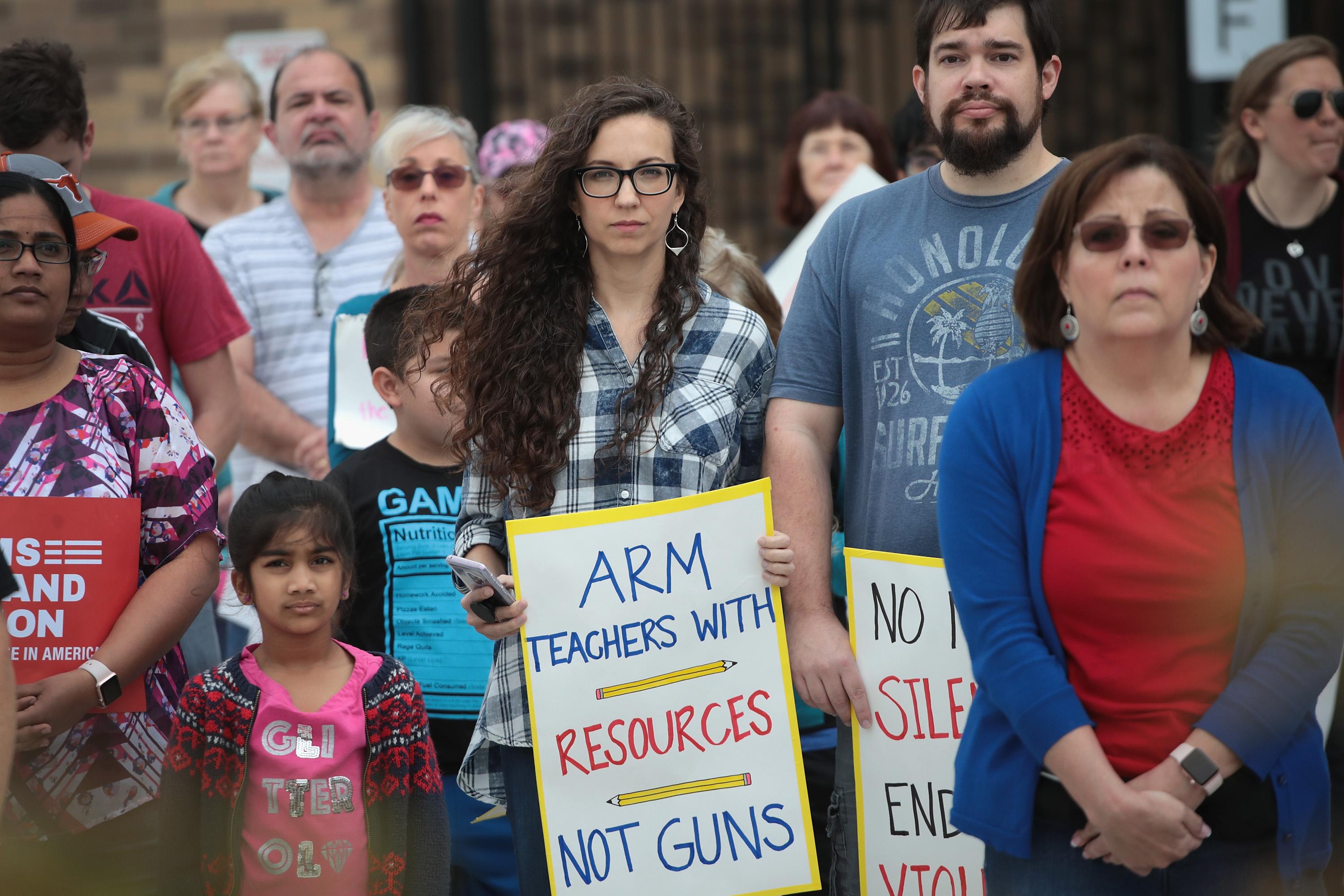 A woman holds a sign reading, "Arm teachers with resources not guns."