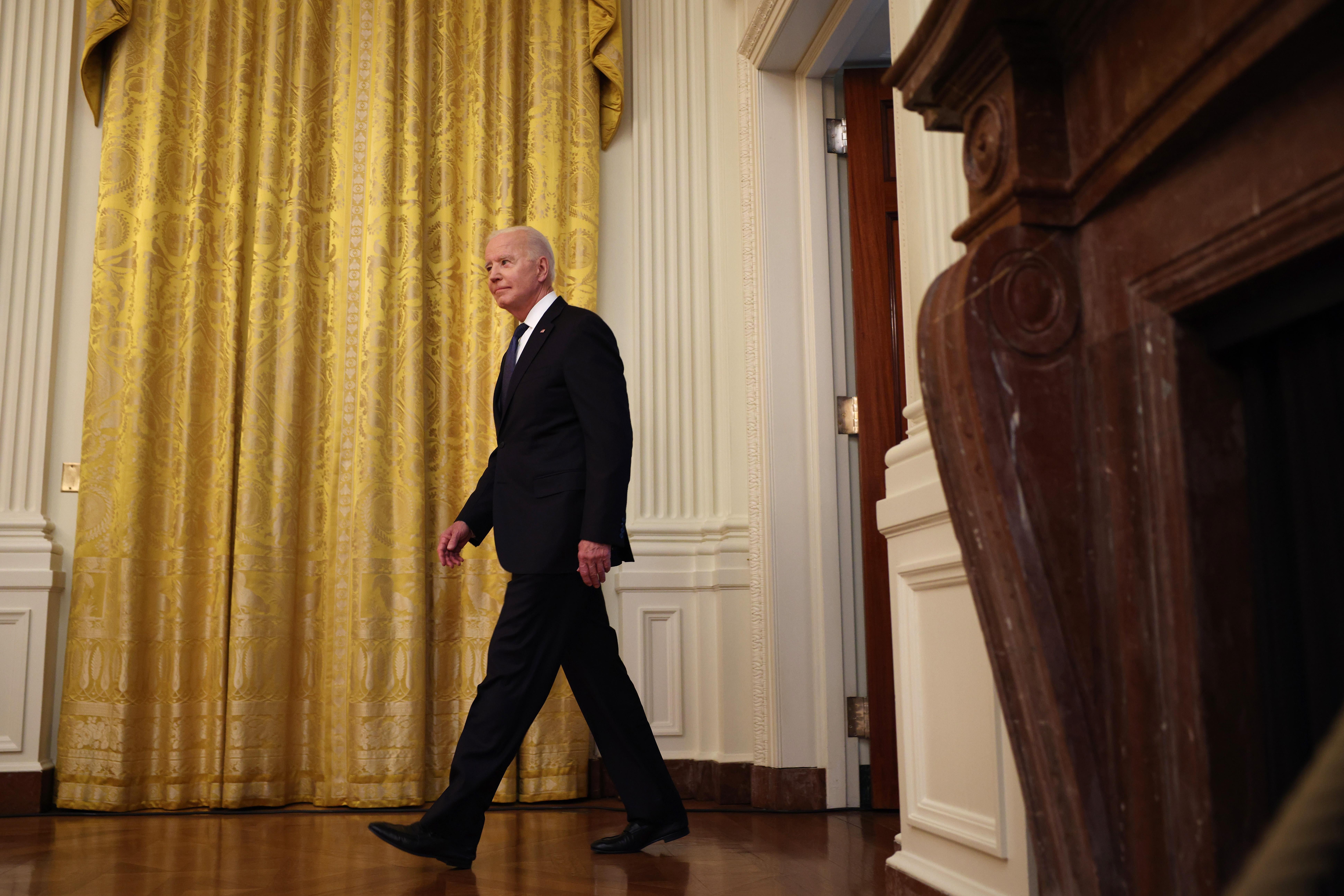 Joe Biden walks into a room in front of a golden curtain.