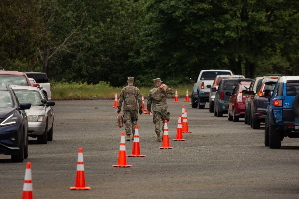 Two guard members walk along a line of orange traffic cones between two rows of idling cars.