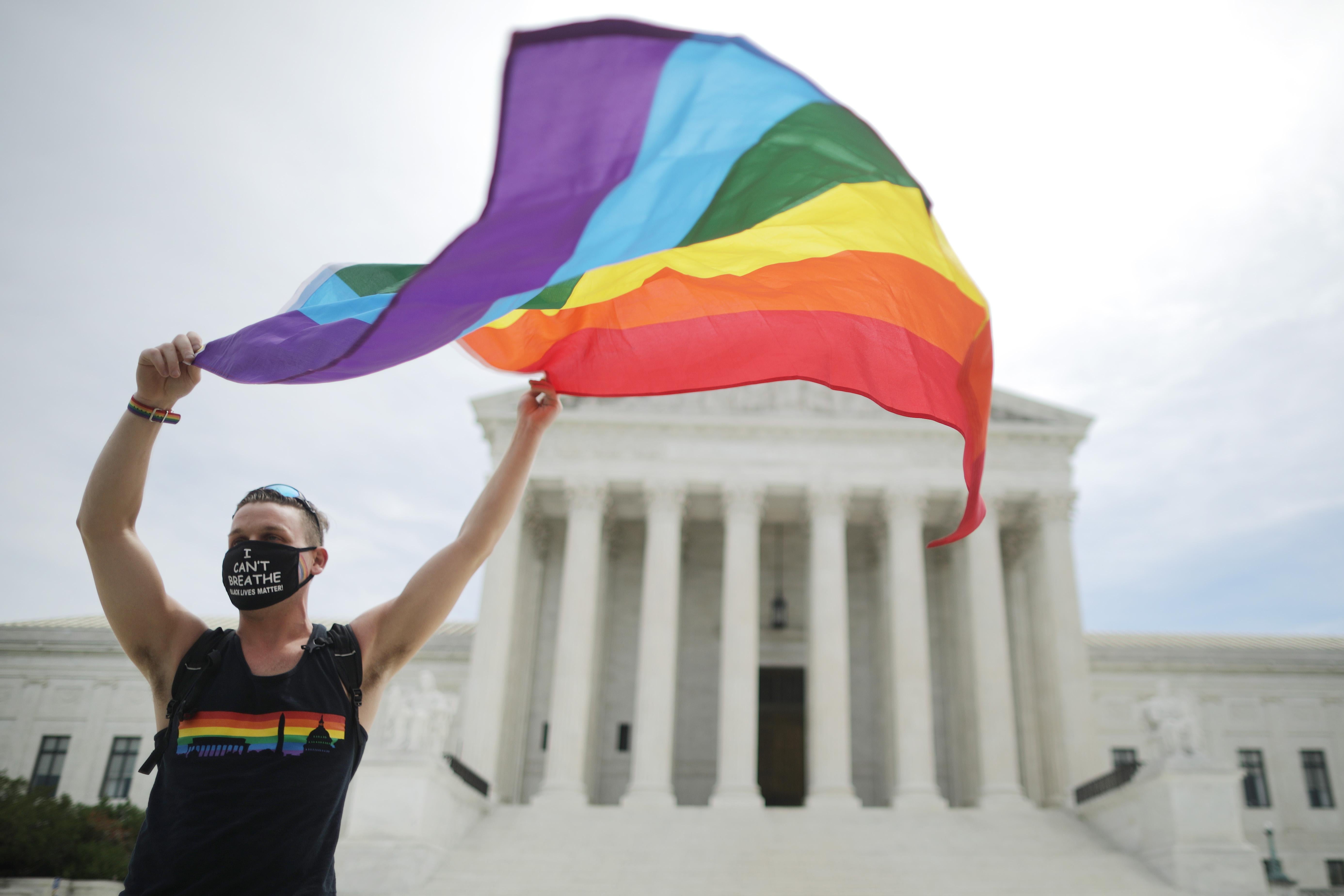 Fons waves a Pride flag and wears a mask that says "I can't breathe" in front of the Supreme Court.