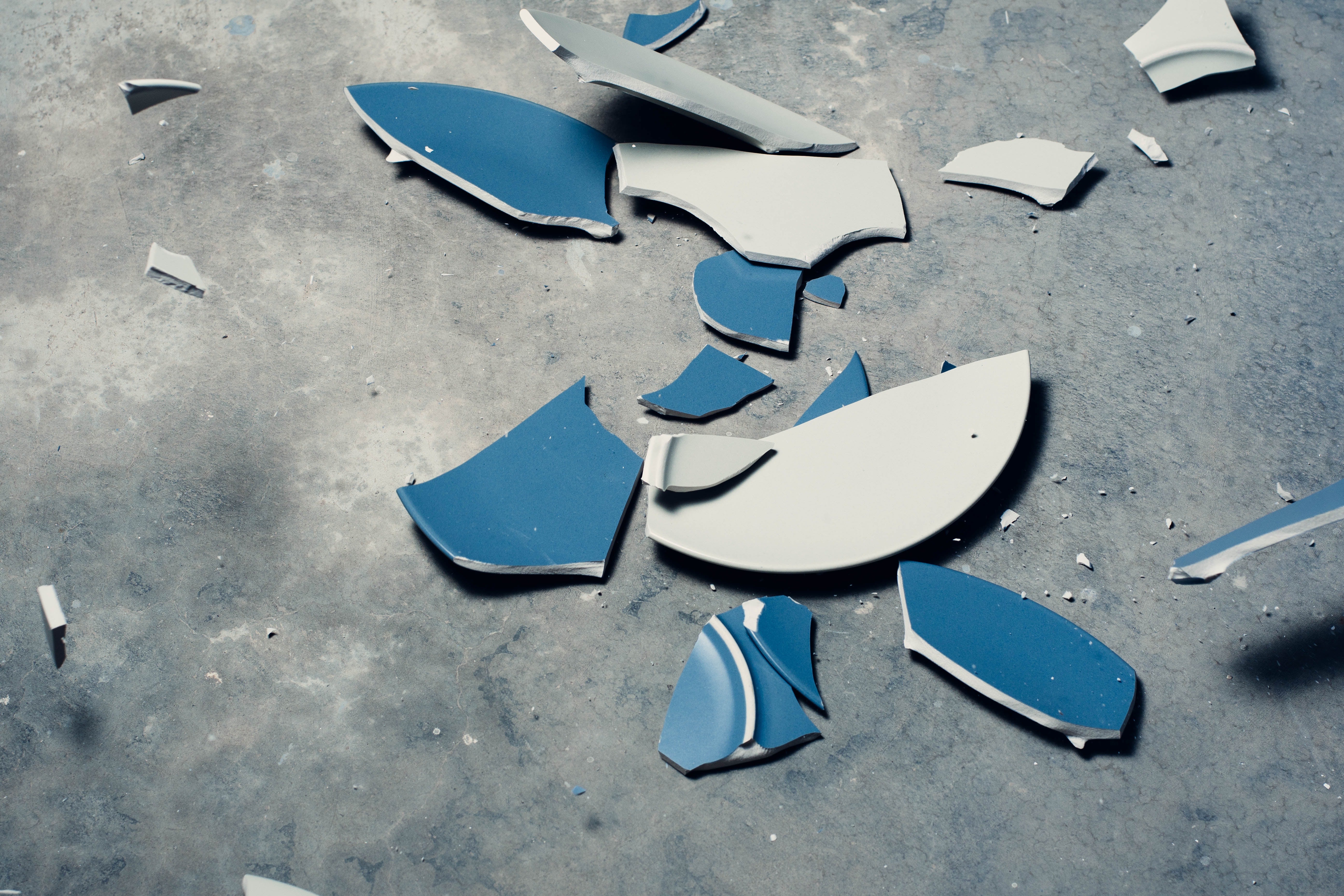 A blue plate shattered in pieces on a concrete floor. 