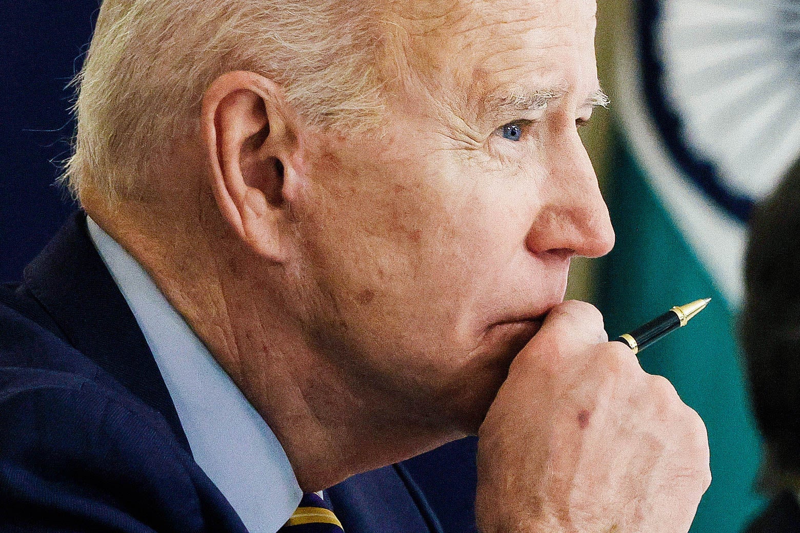 Joe Biden, in profile, holds his hand (with a pen in it) up to his chin.