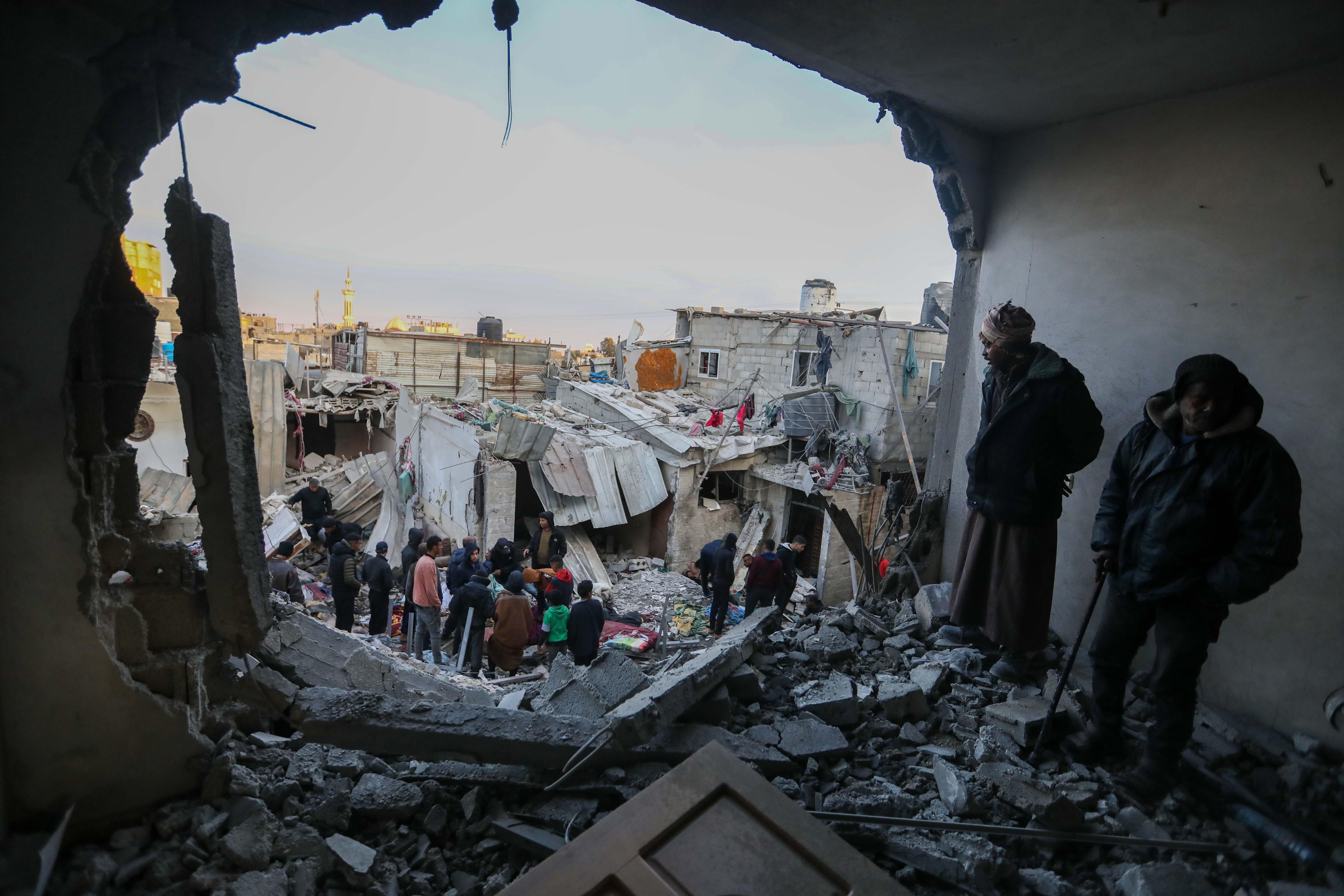 People stand in a building reduced to rubble with a large hole blown through the wall.