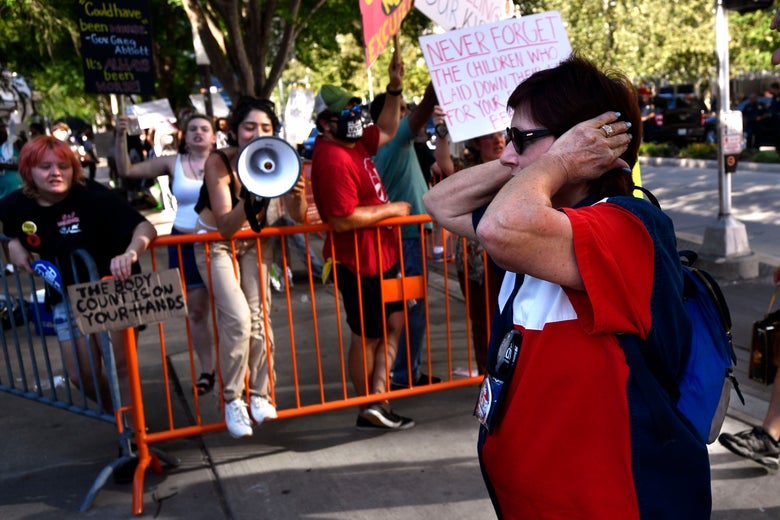 A conventiongoer covers her ears as she walks past people protesting the NRA behind a barrier