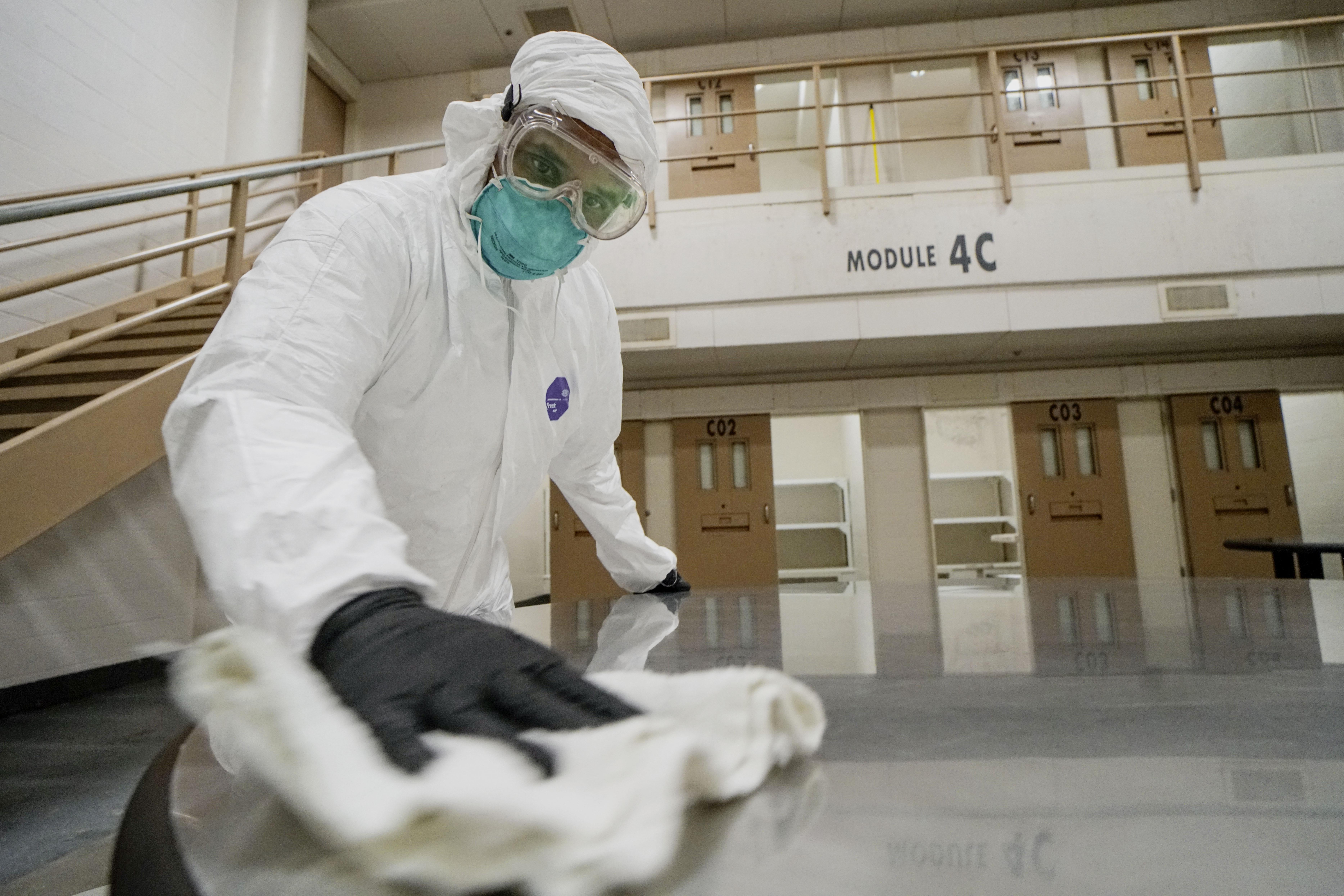 A man in a protective suit, goggles and mask scrubs the floor of a jail.