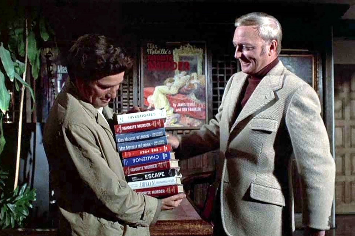 Columbo holds a stack of books, while a man in a suit selects one of the books.