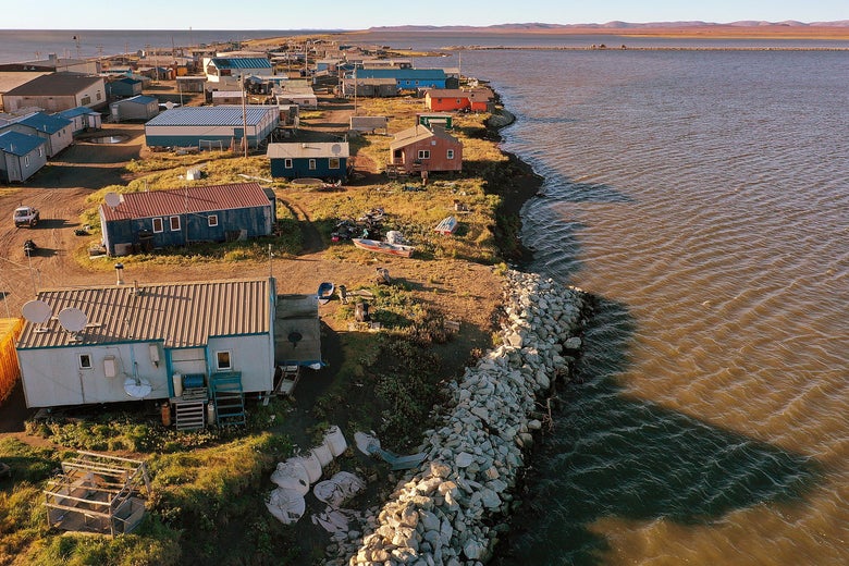 An overhead shot of a small Alaskan village, of small homes with corrugated roofs, on a narrow spit of land extending into the sea.