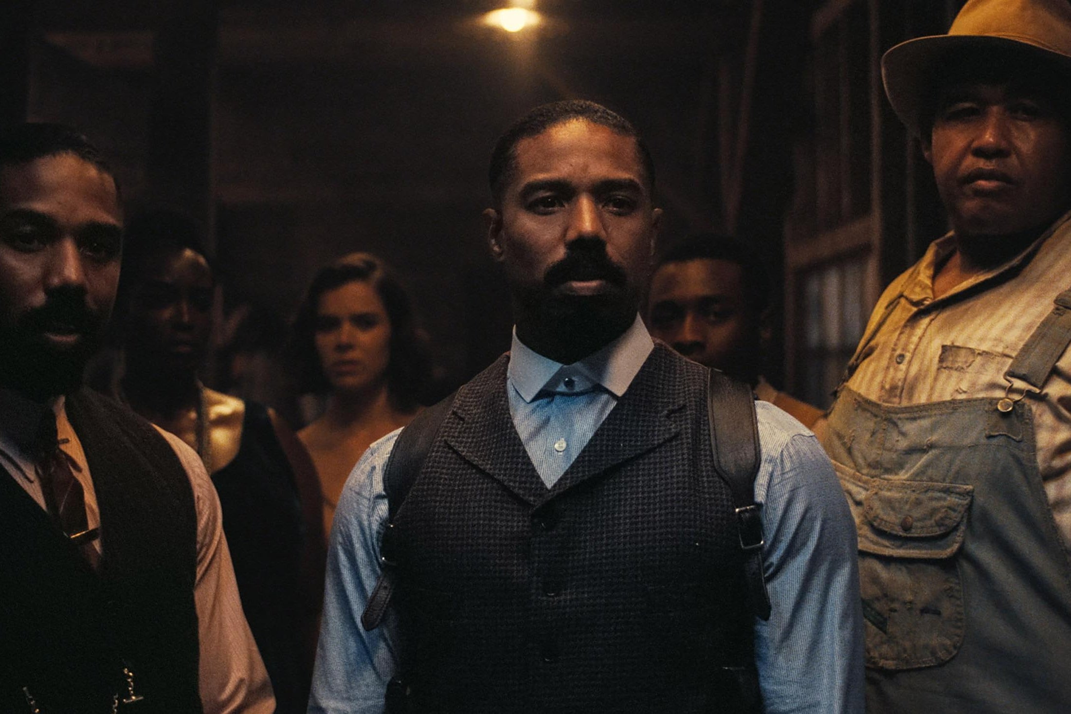 Michael B. Jordan as twins, and other characters, standing at an open door.