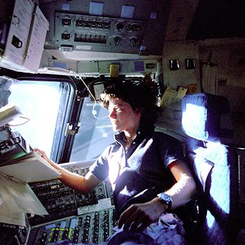 American astronaut Sally K. Ride, mission specialist on STS-7, monitors control panels from the pilot's chair on the Flight Deck, June 25, 1983.