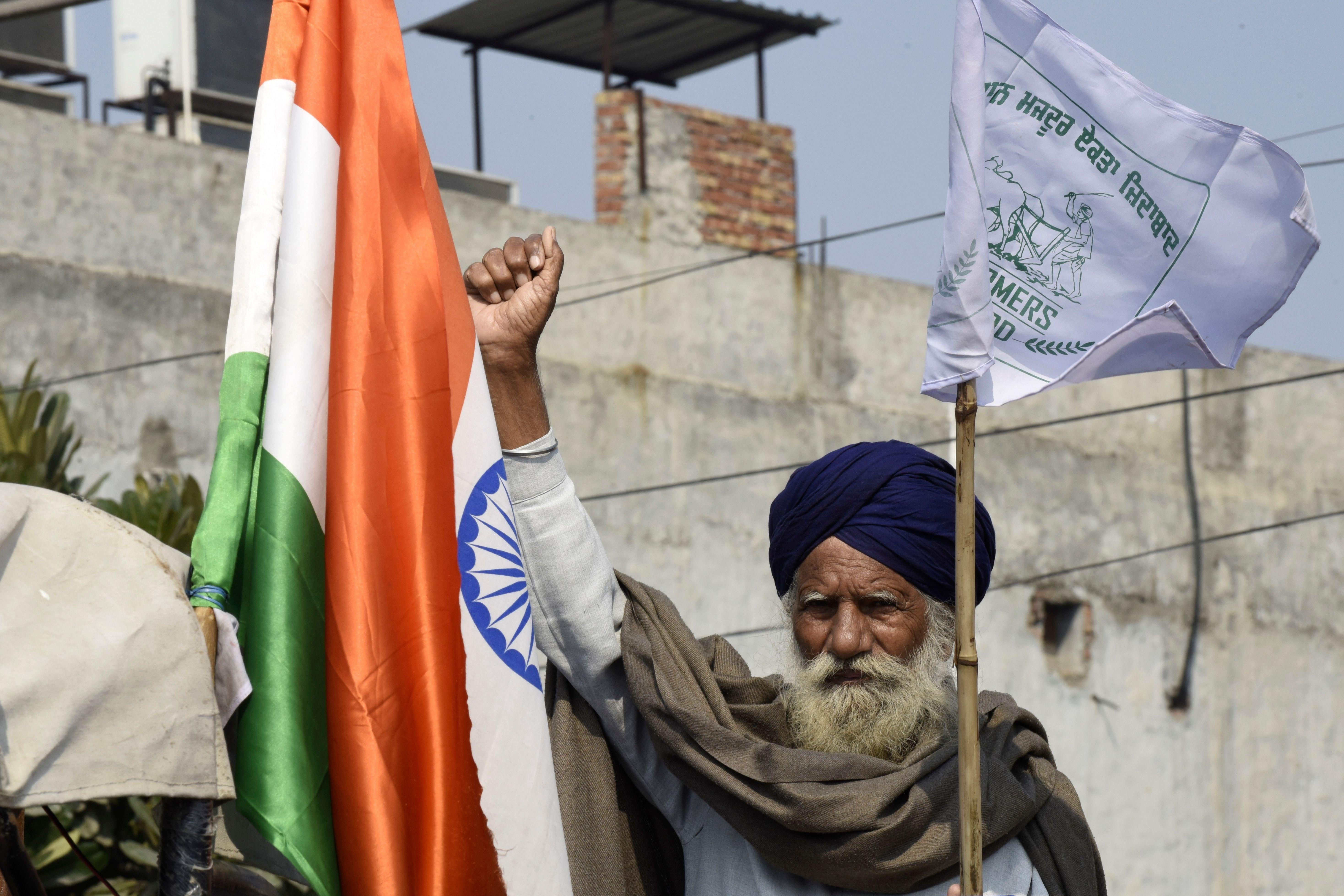 A Sikh man raises his fist and carries a flag next to an Indian flag.