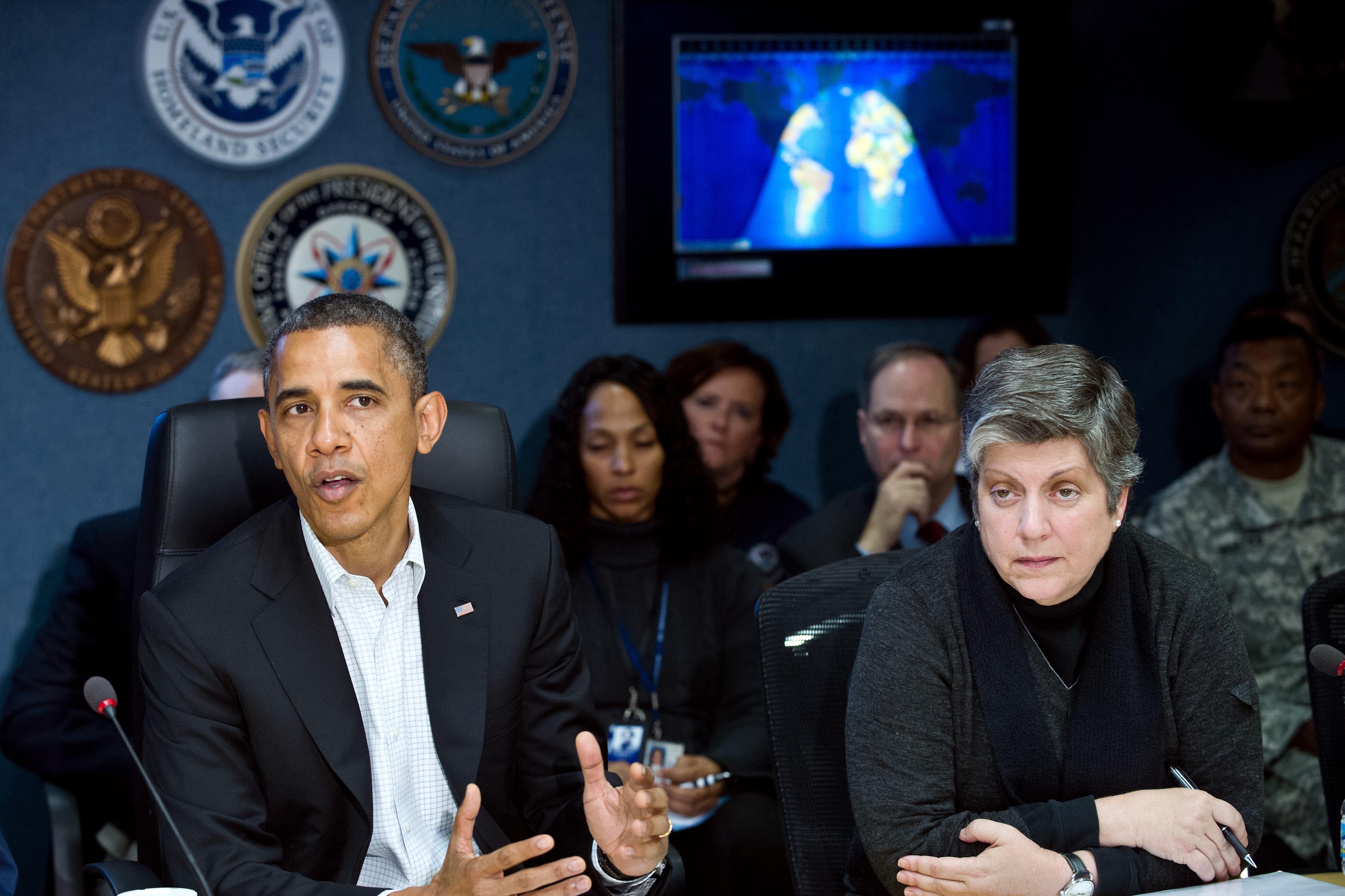 Obama speaks as Napolitano sits next to him at a conference table. A map is projected behind them.
