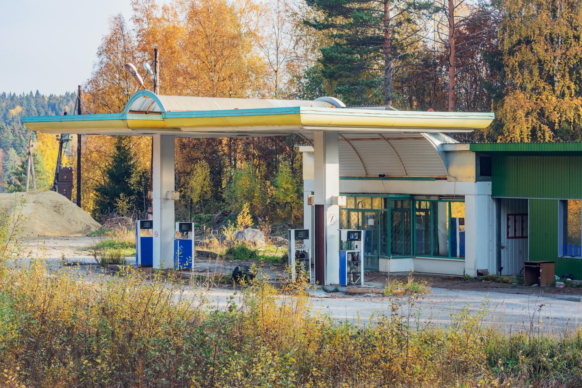 A charming old-fashioned gas station sits empty against a scenic backdrop of mountains with changing autumn leaves. 